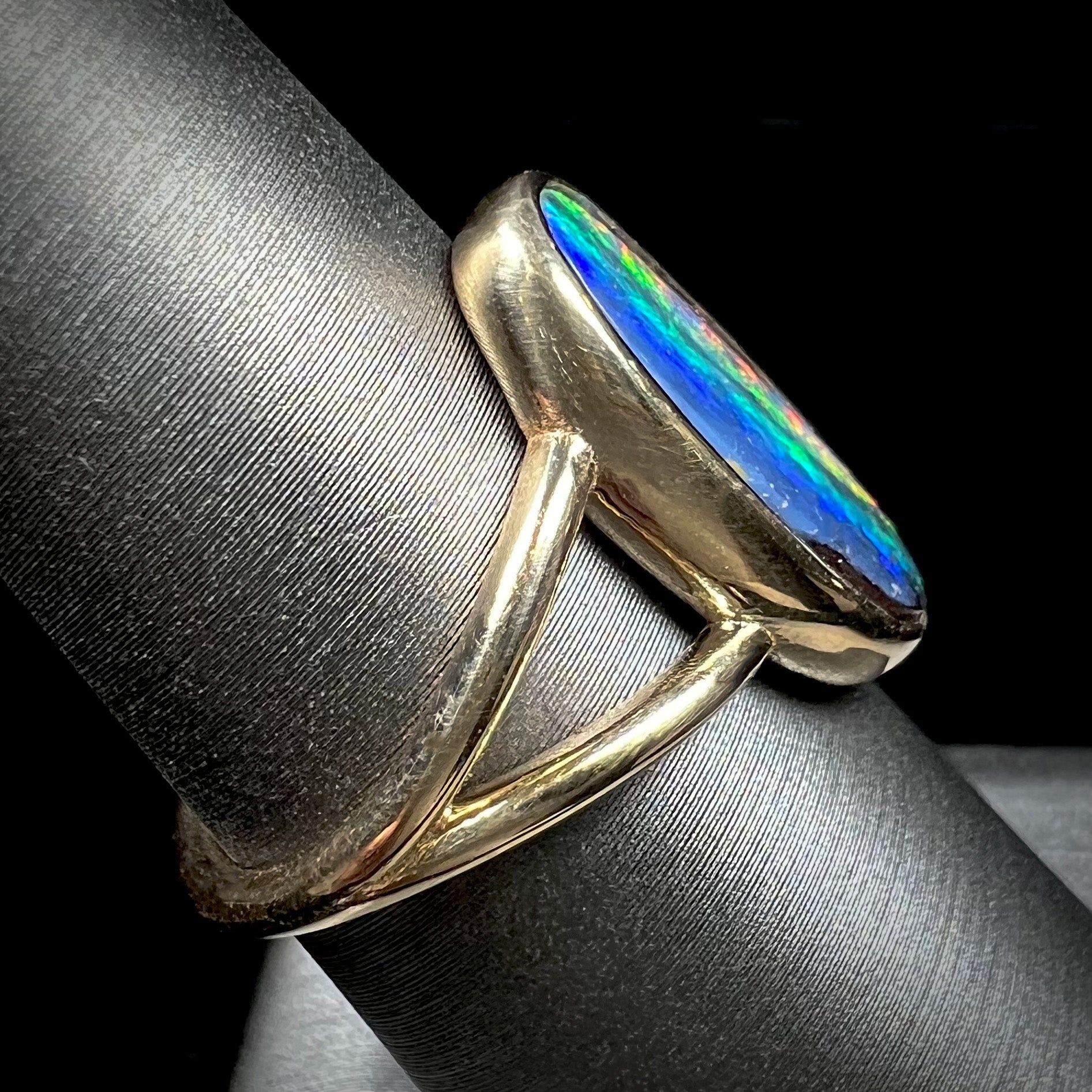 A ladies' yellow gold split shank solitaire ring set with a natural Australian black boulder opal.