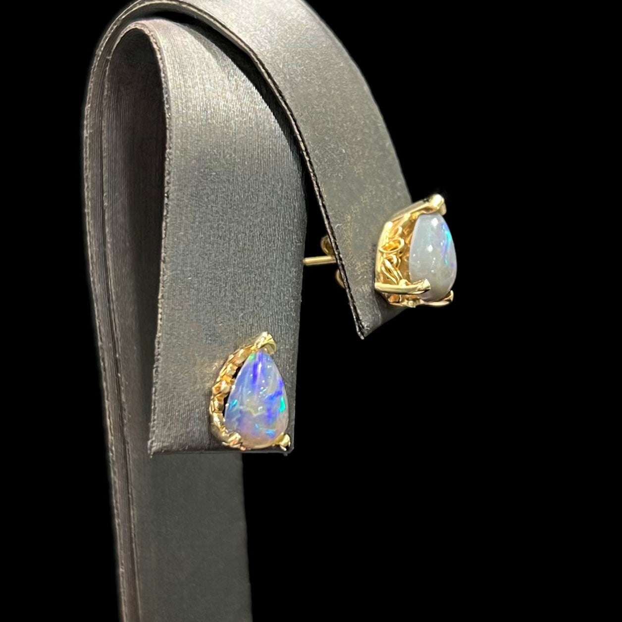 A pair of pear shaped natural black opal stud earrings in filigree style yellow gold baskets.