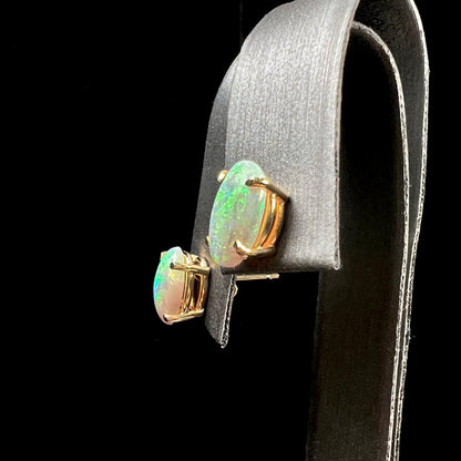 A pair of natural, semi-black crystal opal stud earrings in yellow gold.  The opals are oval cabochon cut.