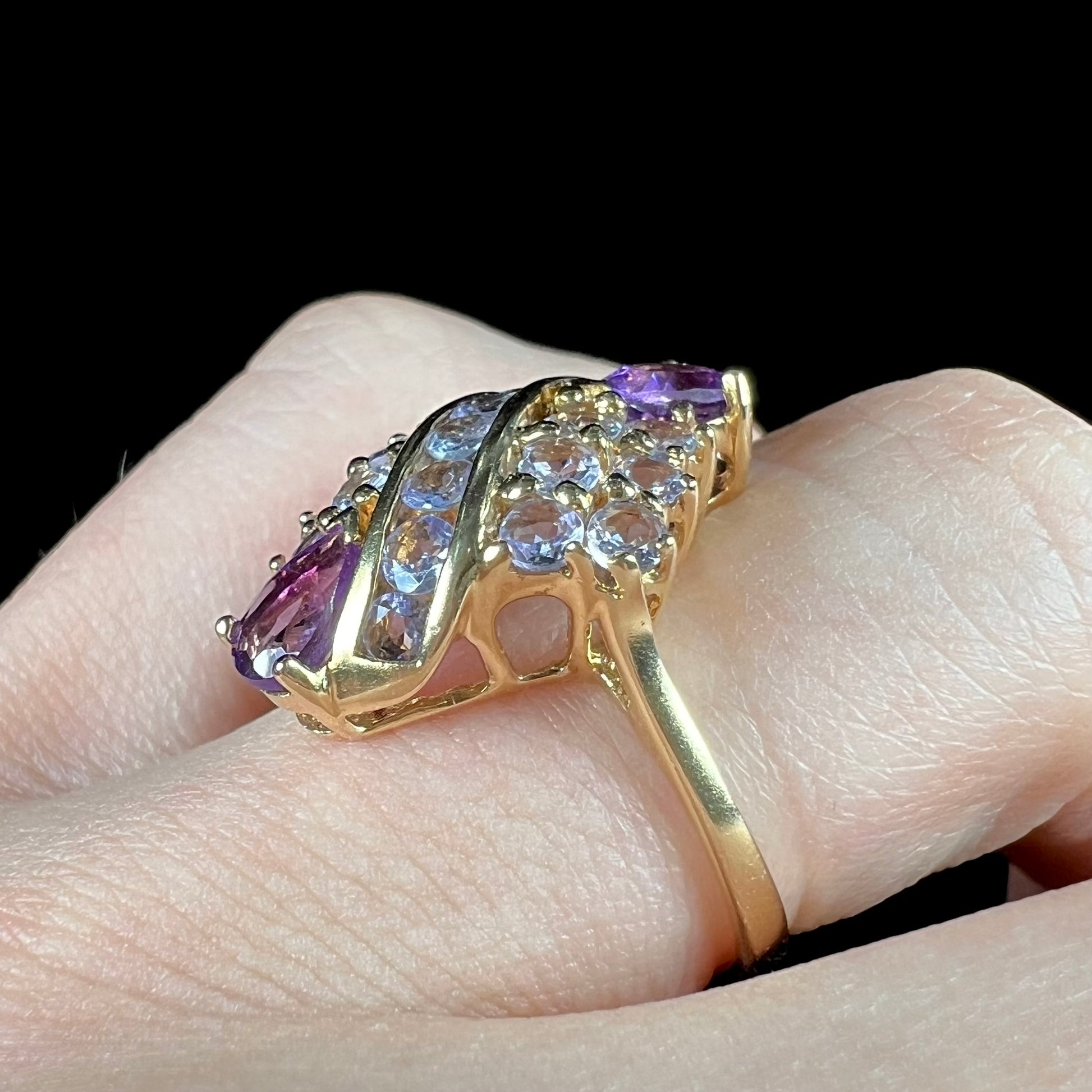 A ladies' gold ring set with a cluster of round tanzanites and two pear shaped amethyst accent stones.