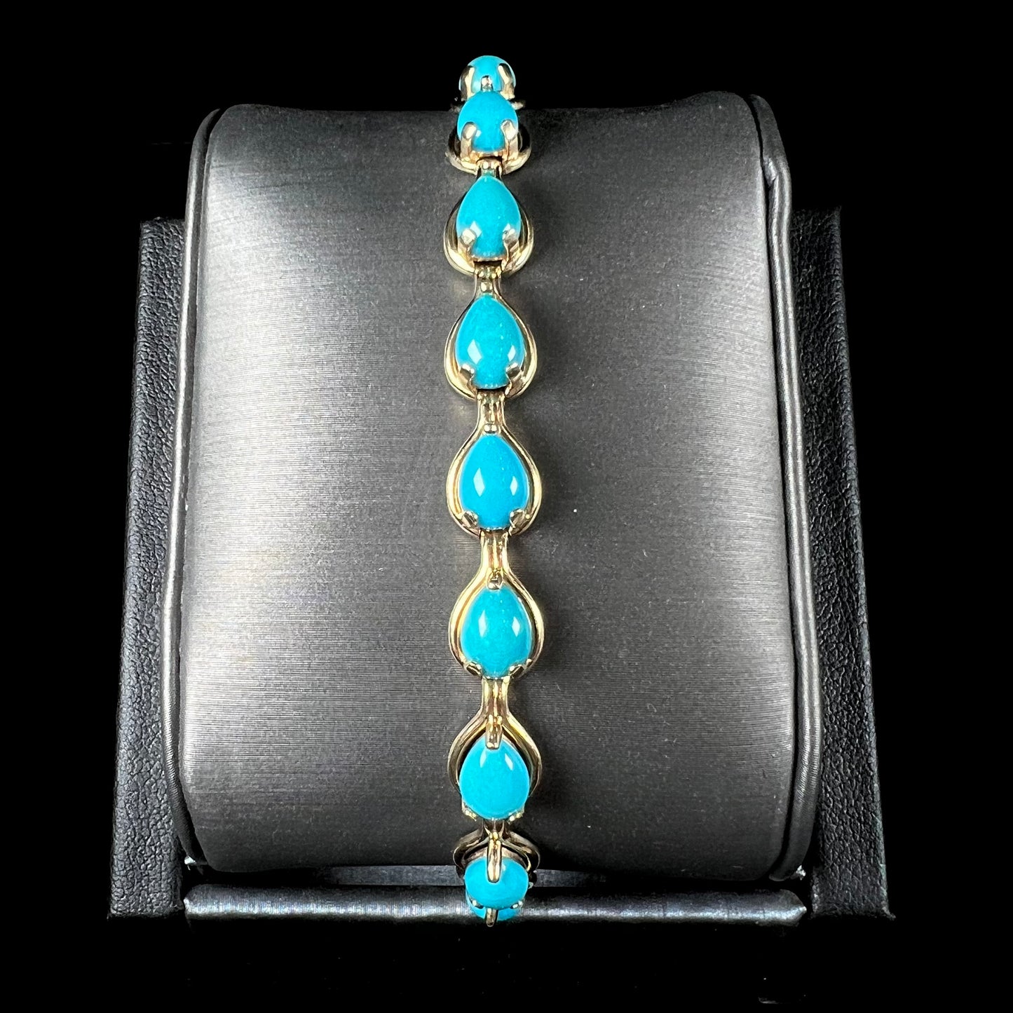 A ladies' yellow gold tennis style bracelet set with pear cabochon shaped natural Sleeping Beauty turquoise stones.