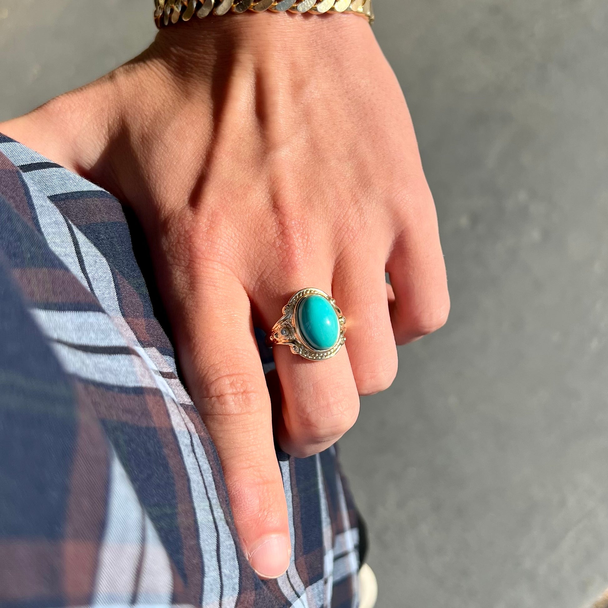 A yellow gold ring set with a greenish blue Sleeping Beauty turquoise cabochon with two diamond accents.