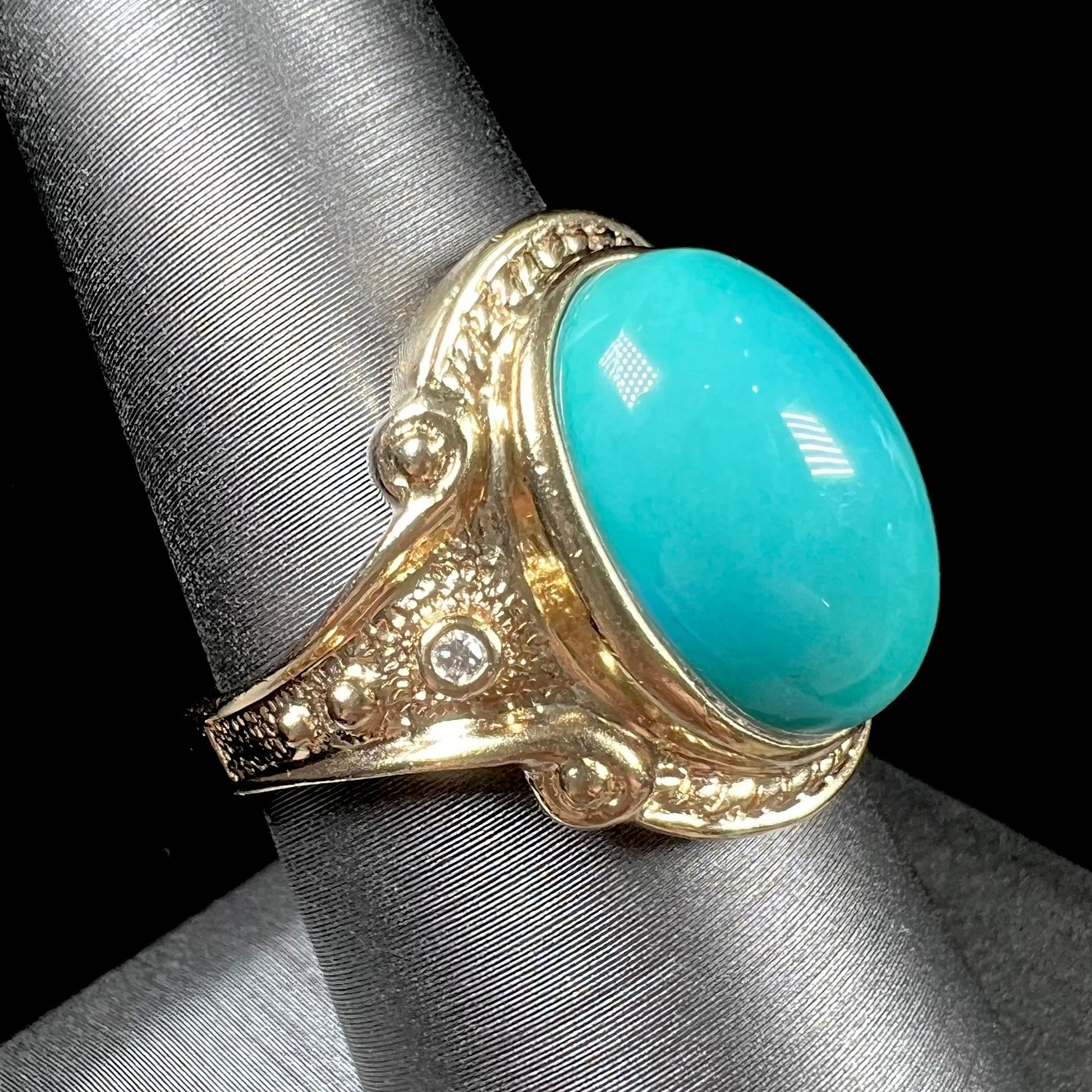 A yellow gold ring set with a greenish blue Sleeping Beauty turquoise cabochon with two diamond accents.