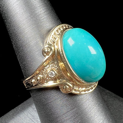 A yellow gold ring set with a greenish blue Sleeping Beauty turquoise cabochon with two diamond accents.