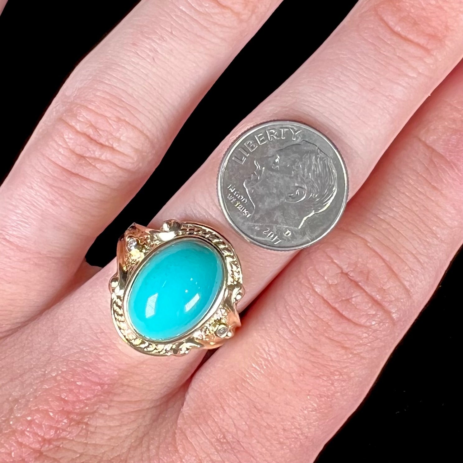 A yellow gold ring set with a greenish blue Sleeping Beauty turquoise cabochon with two diamond accents.