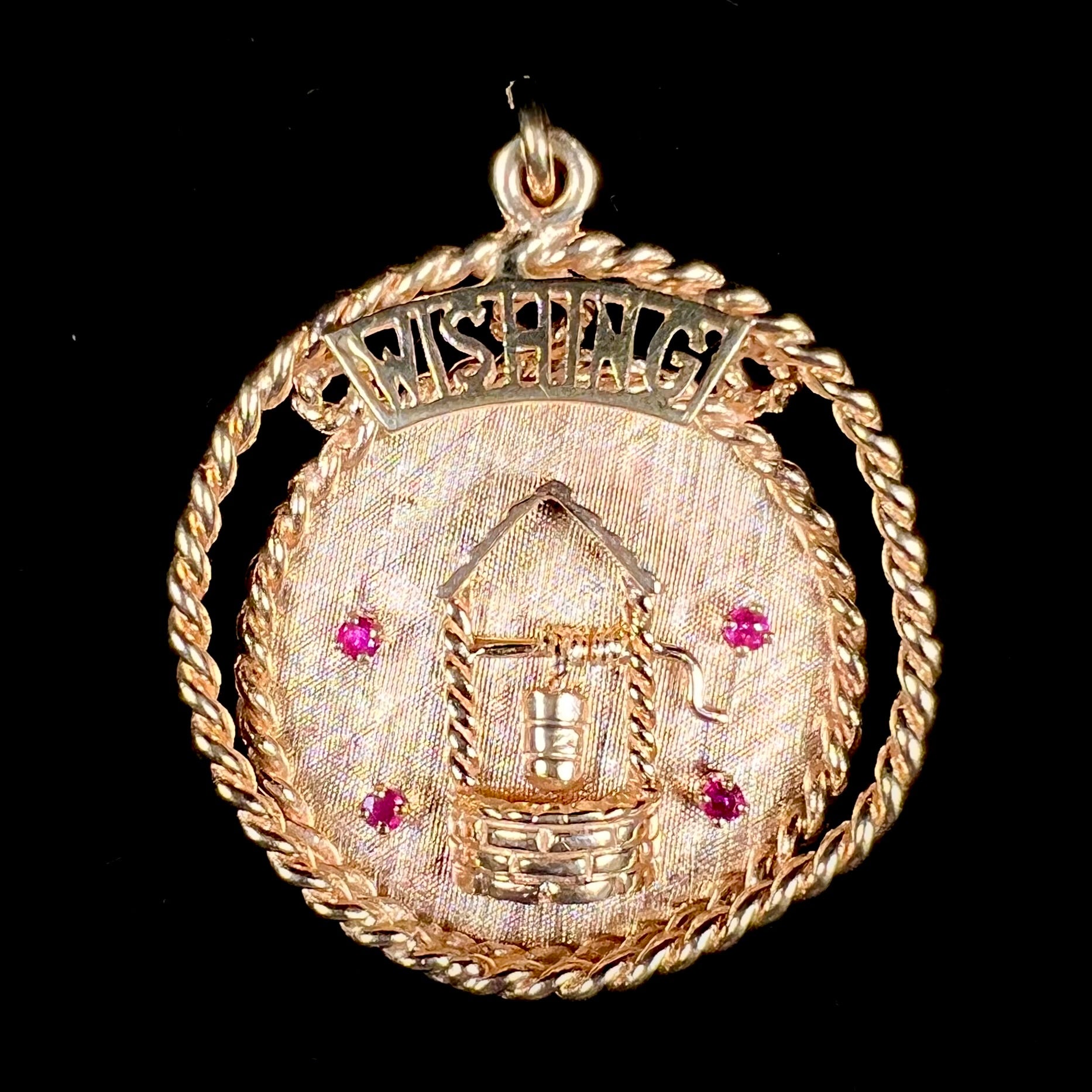 A yellow gold pendant depicting a picture of a wishing well, set with four natural rubies.  The word "WISHING" sits at the top of the pendant.