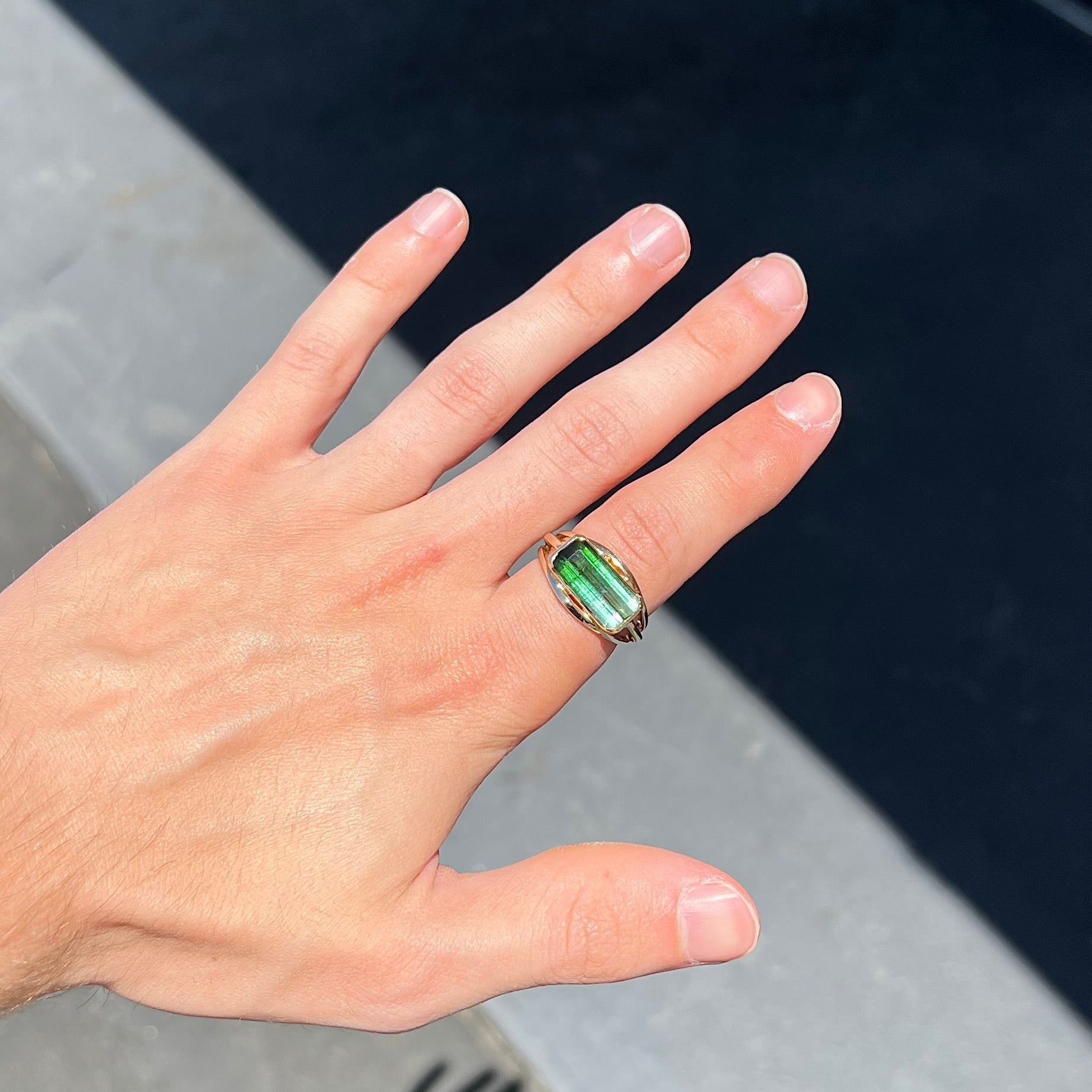 A men's emerald cut tricolor tourmaline solitaire ring in yellow gold.  The tourmaline shifts from green to blue green to blue.