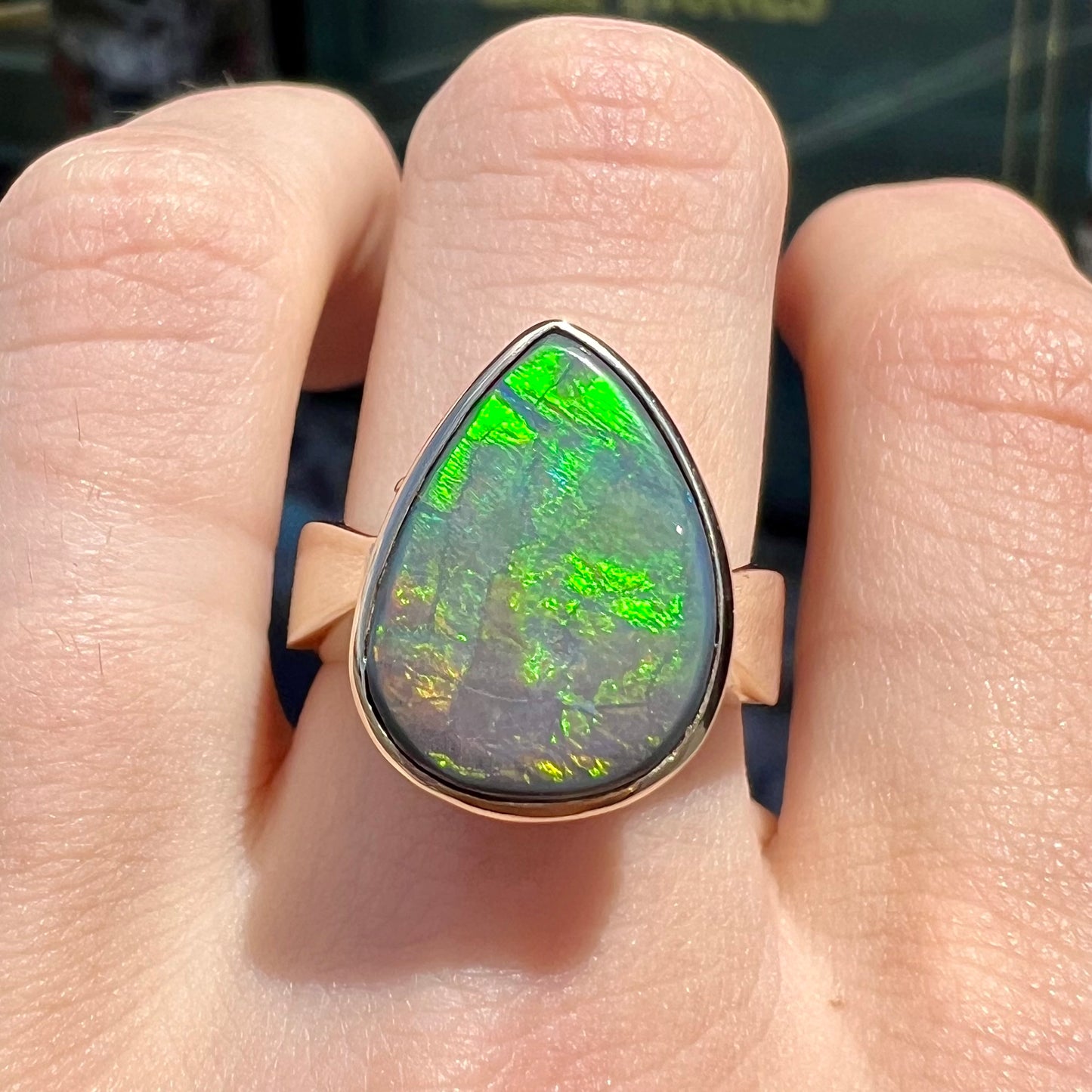 A large ladies' yellow gold solitaire ring set with a natural, pear shaped black crystal opal.  The opal has green and orange fire.