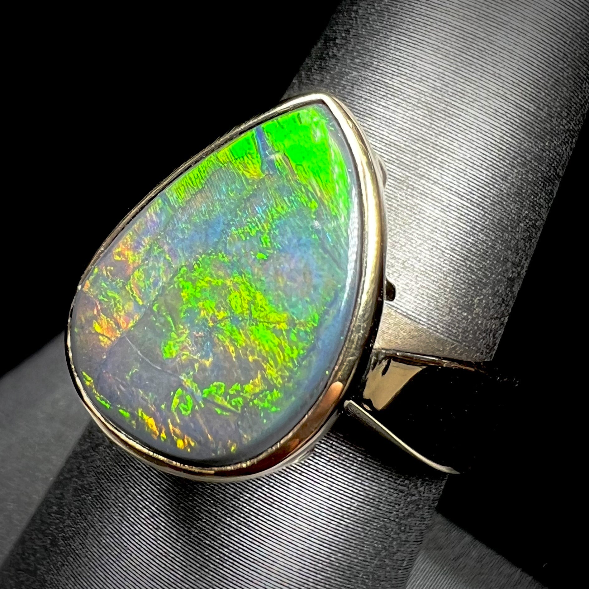A large ladies' yellow gold solitaire ring set with a natural, pear shaped black crystal opal.  The opal has green and orange fire.