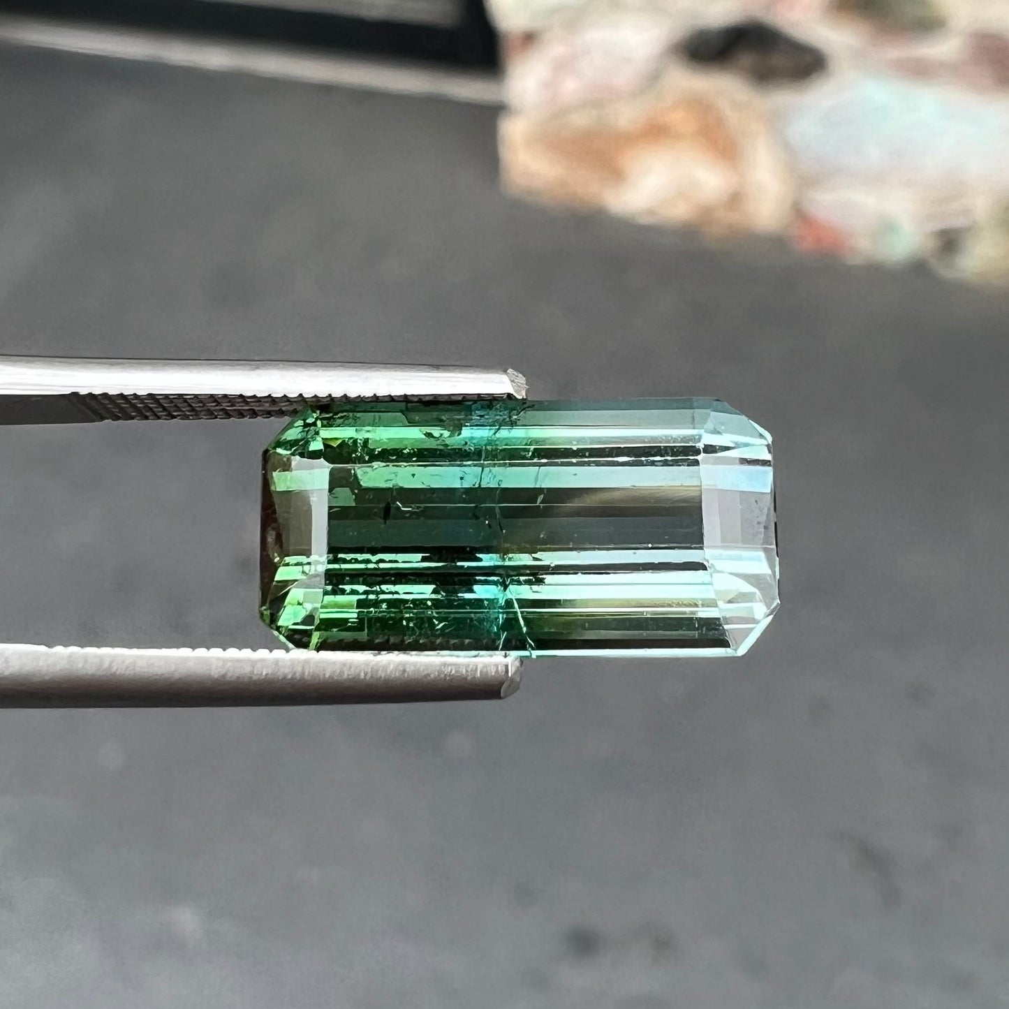 A loose, emerald cut bicolor tourmaline stone.  The colors blend from green to blue-green to sttel blue.