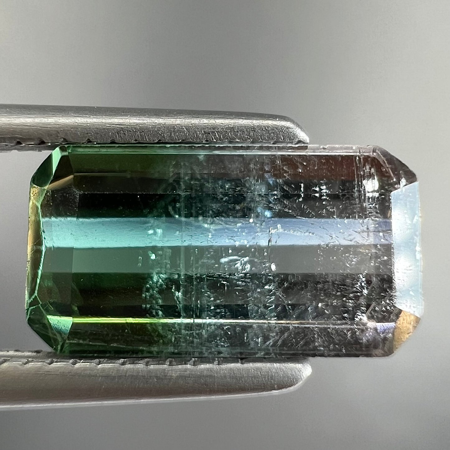 A loose, emerald cut tricolor tourmaline gemstone.  The stone transitions from green to blue to white colors.