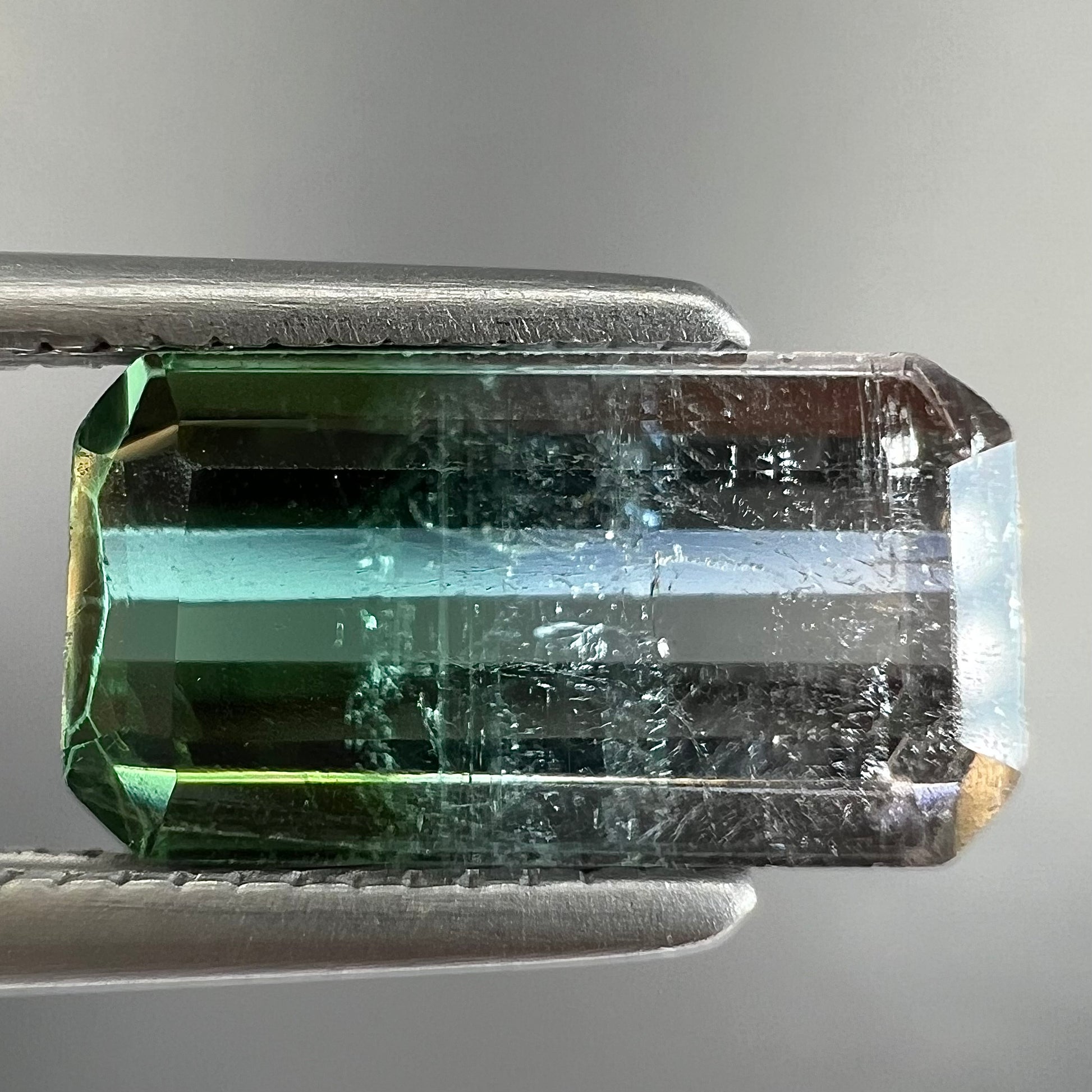 A loose, emerald cut tricolor tourmaline gemstone.  The stone transitions from green to blue to white colors.