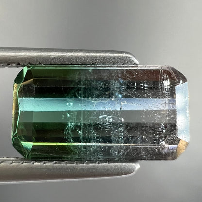 A loose, emerald cut tricolor tourmaline gemstone.  The stone transitions from green to blue to white colors.