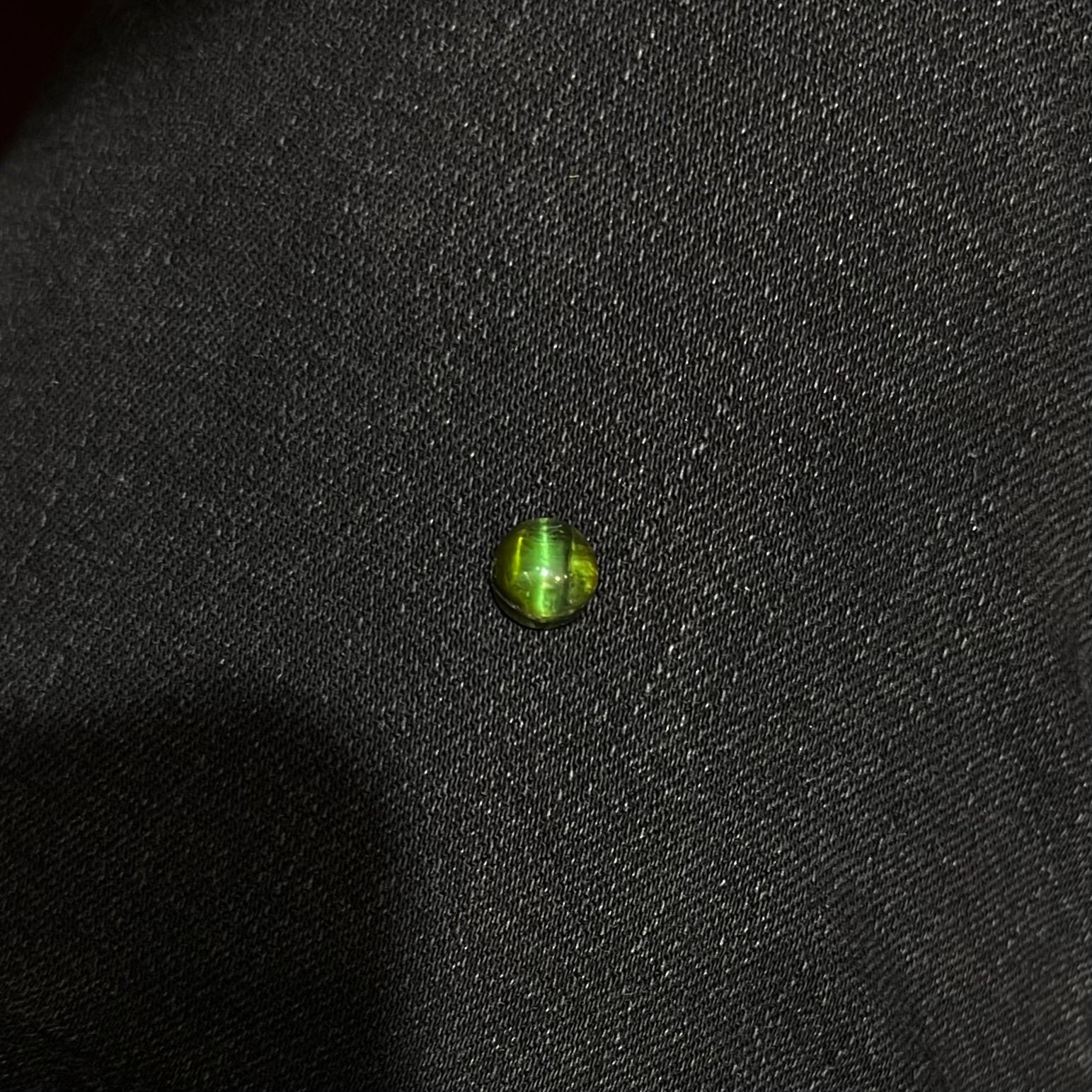 A loose, round cabochon cut green tourmaline stone that displays a cat's eye phenomenon.