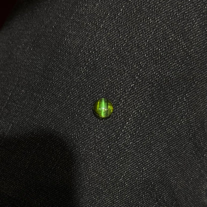 A loose, round cabochon cut green tourmaline stone that displays a cat's eye phenomenon.