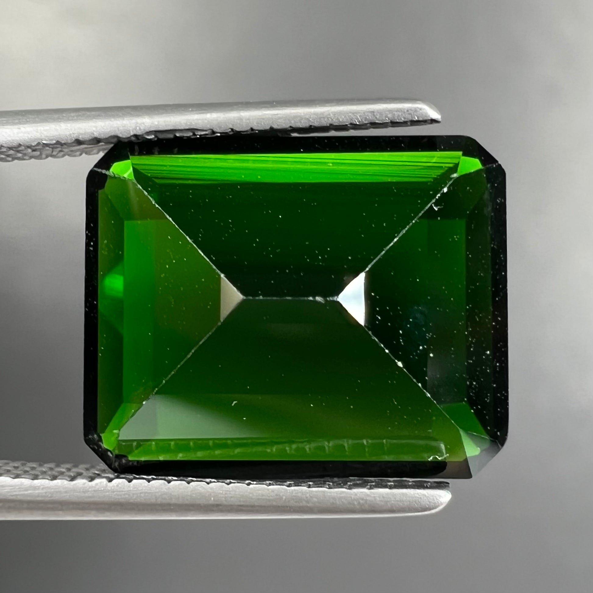 A large, emerald cut chrome diopside gemstone.  The gem is dark green color.