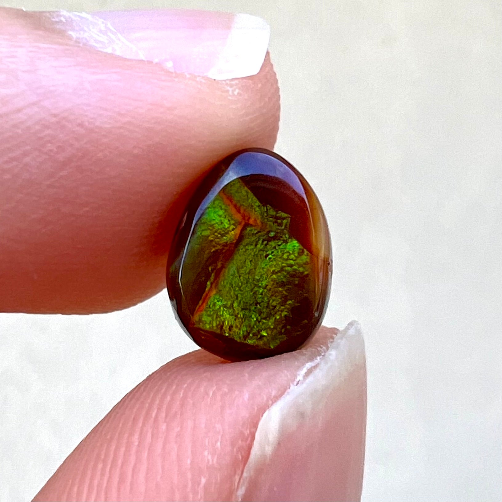 A loose, pear shaped Mexican fire agate cabochon.  The stone is glittery green with an orange streak.