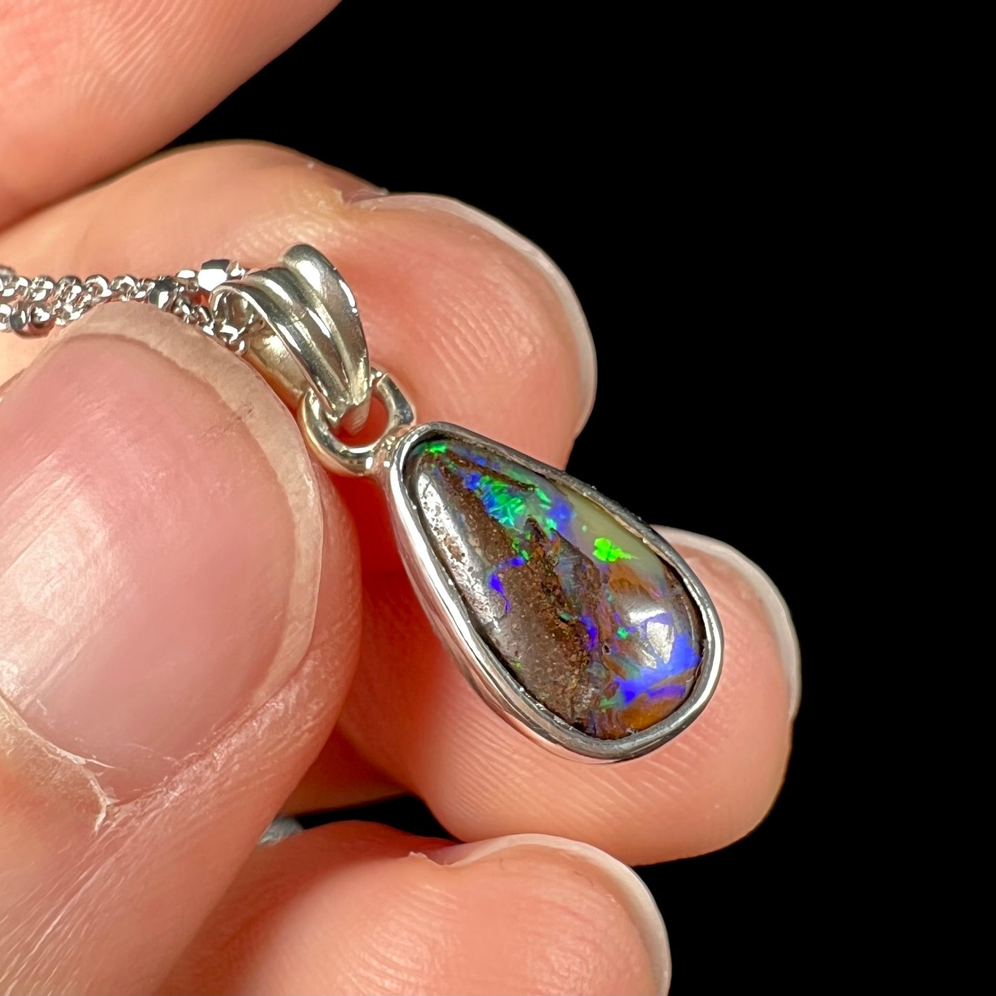 A natural, pear shaped Australian boulder opal with blue, purple, and green colors bezel set into a sterling silver necklace.