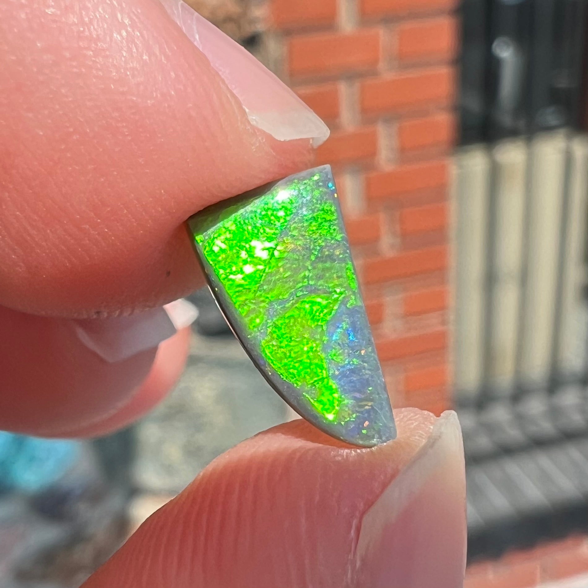 A loose, triangular shaped black opal stone from Lightning Ridge, Australia.  The opal has a bright green flash of color.