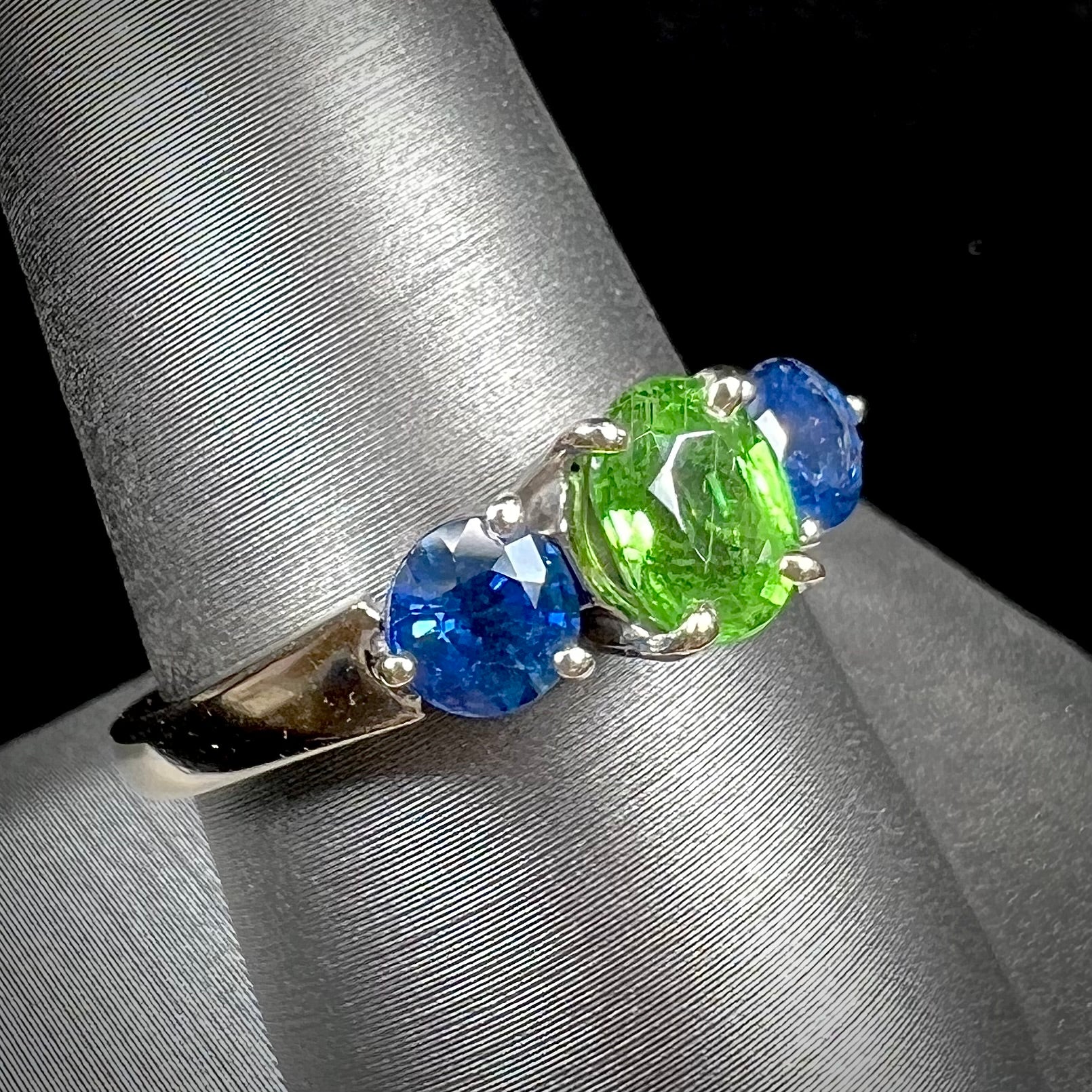 A ladies' white gold three stone ring set with two round blue sapphires and an oval cut green tsavorite garnet.