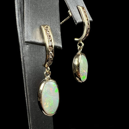 A pari of yellow gold dangle earrings set with natural white crystal opals and diamond accents.