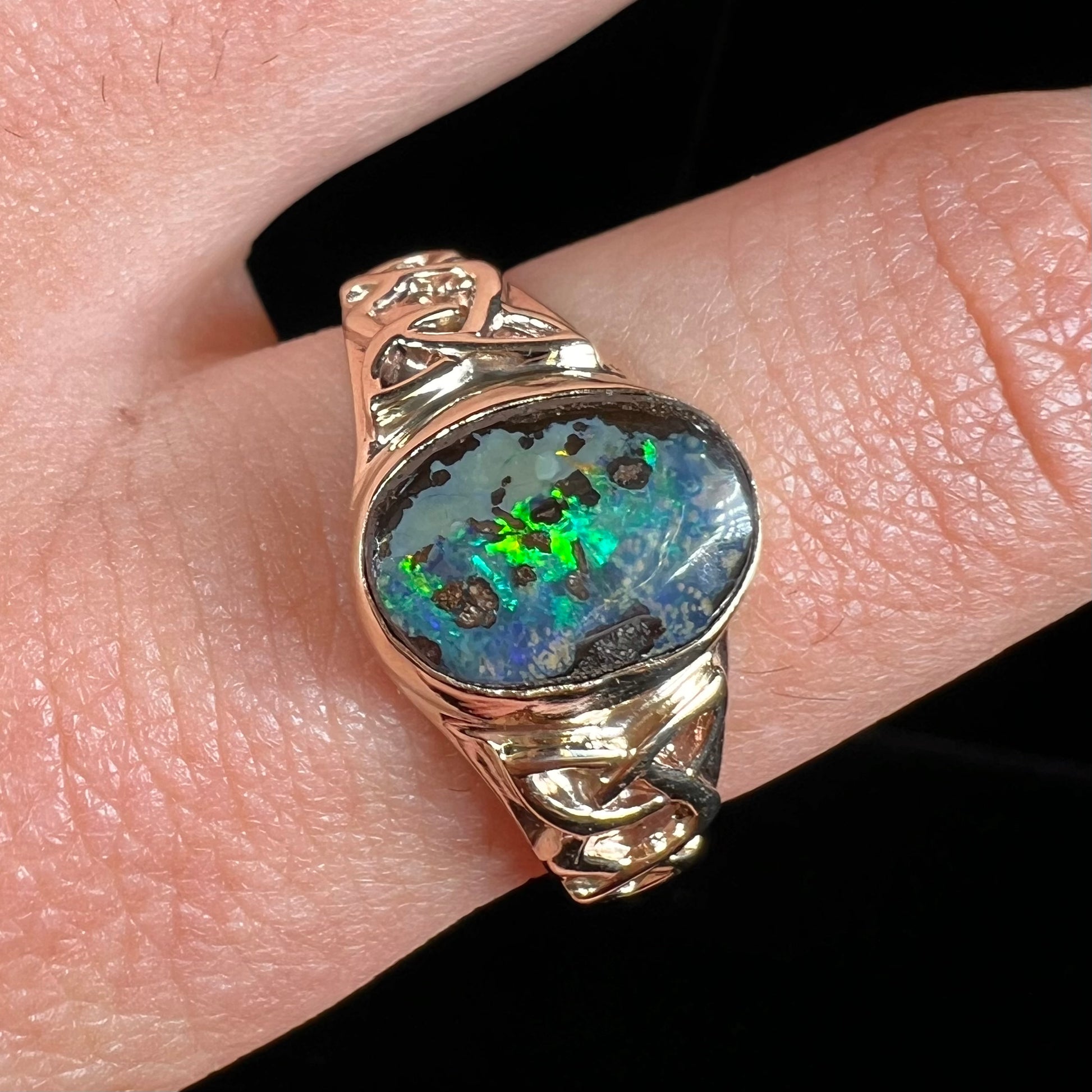 A unisex Celtic style natural boulder opal ring cast in yellow gold.  The opal shines green and blue.