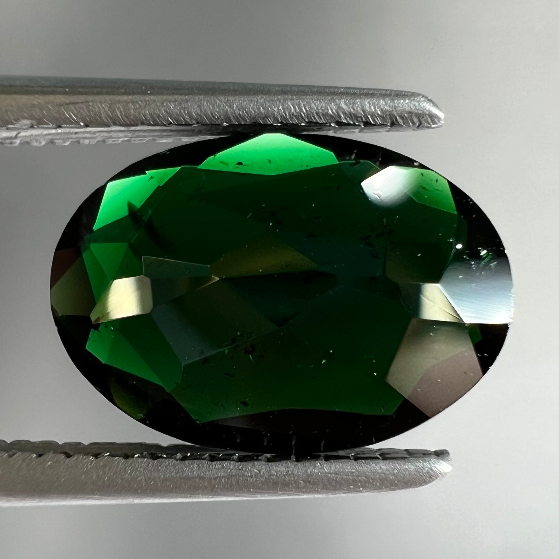A faceted oval cut chrome tourmaline gemstone.  The stone is dark green.