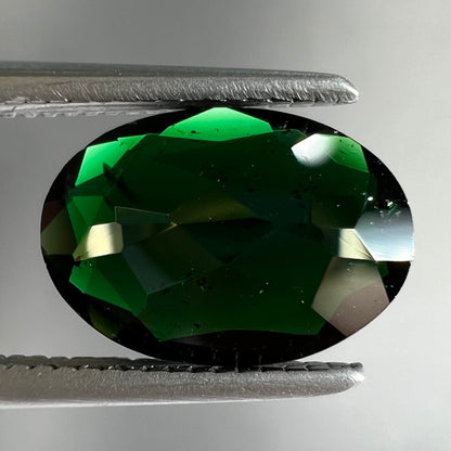 A faceted oval cut chrome tourmaline gemstone.  The stone is dark green.