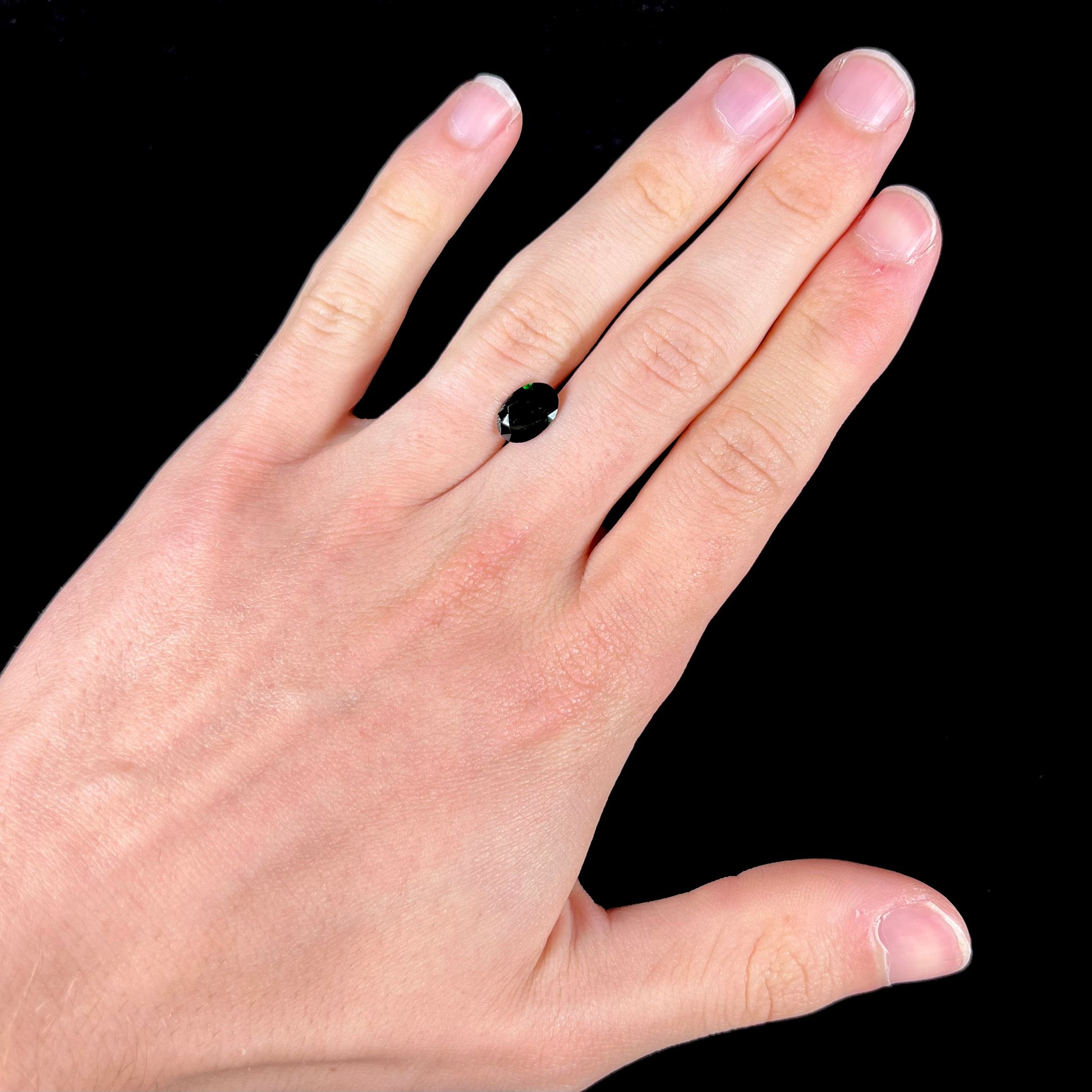 A faceted oval cut chrome tourmaline gemstone.  The stone is dark green.