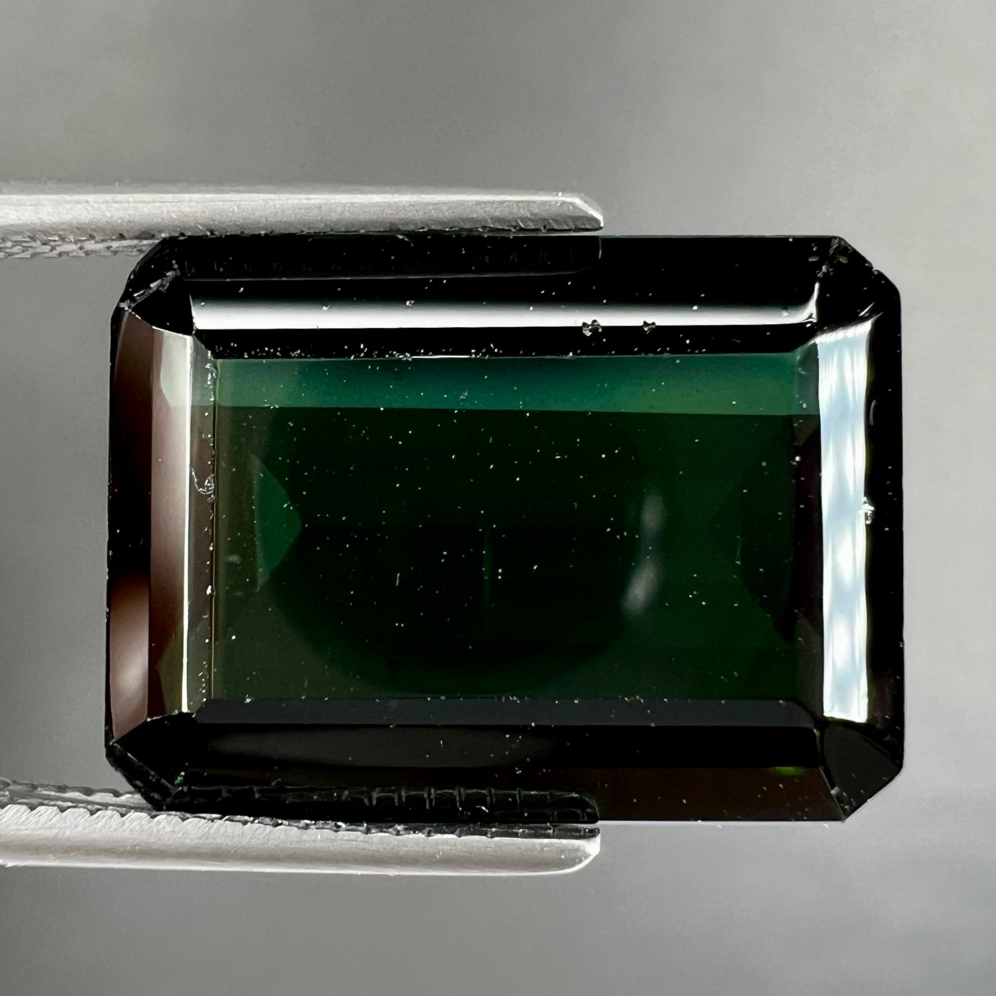 A faceted emerald cut dark green tourmaline gemstone.