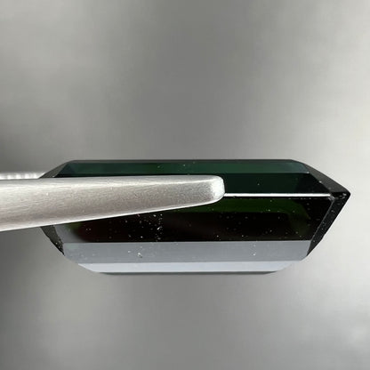 A faceted emerald cut dark green tourmaline gemstone.