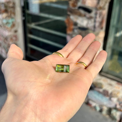 A rectangular step-cut yellowish green tourmaline gemstone.