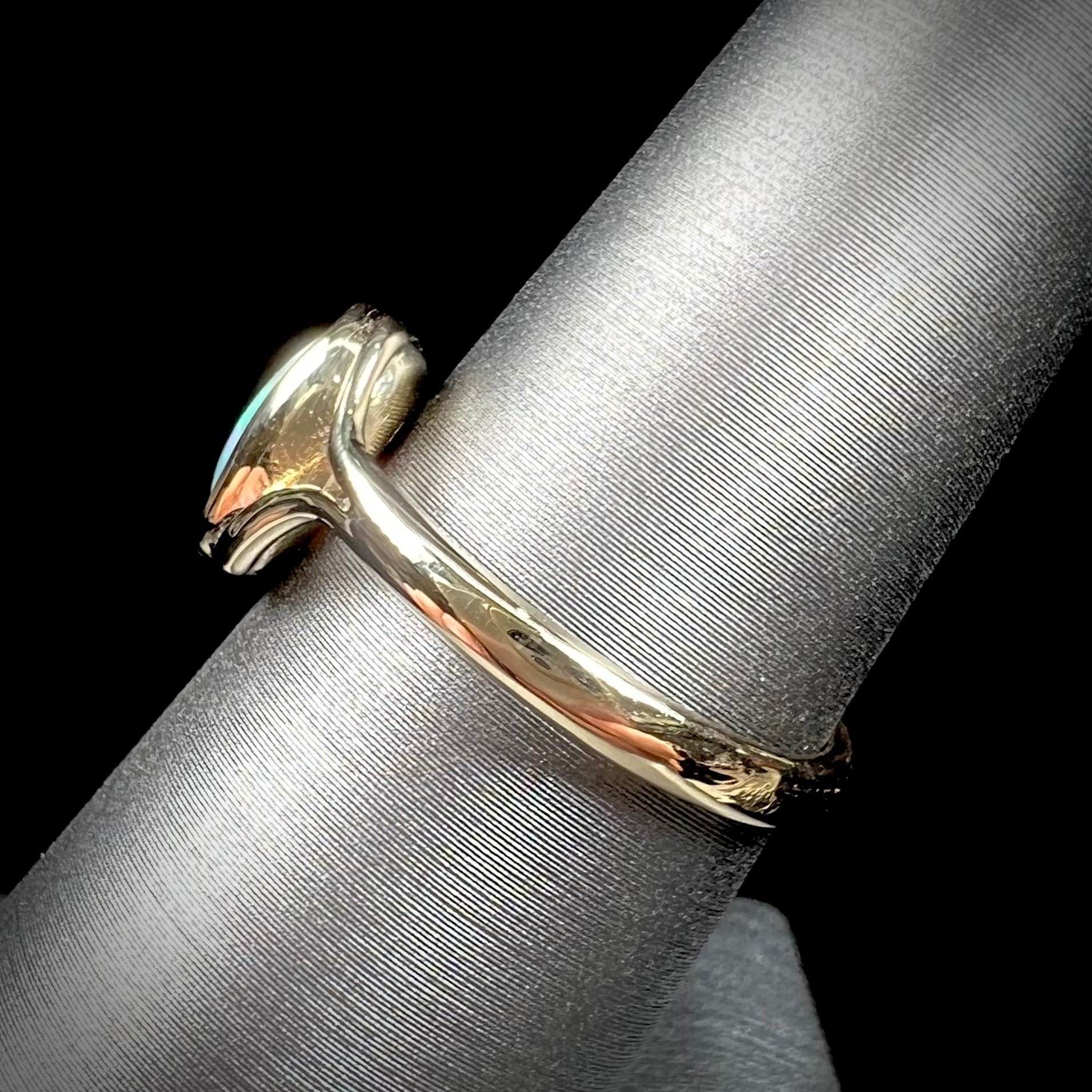 A ladies' oval cut black crystal opal solitaire ring handmade with a single split shank in yellow gold.