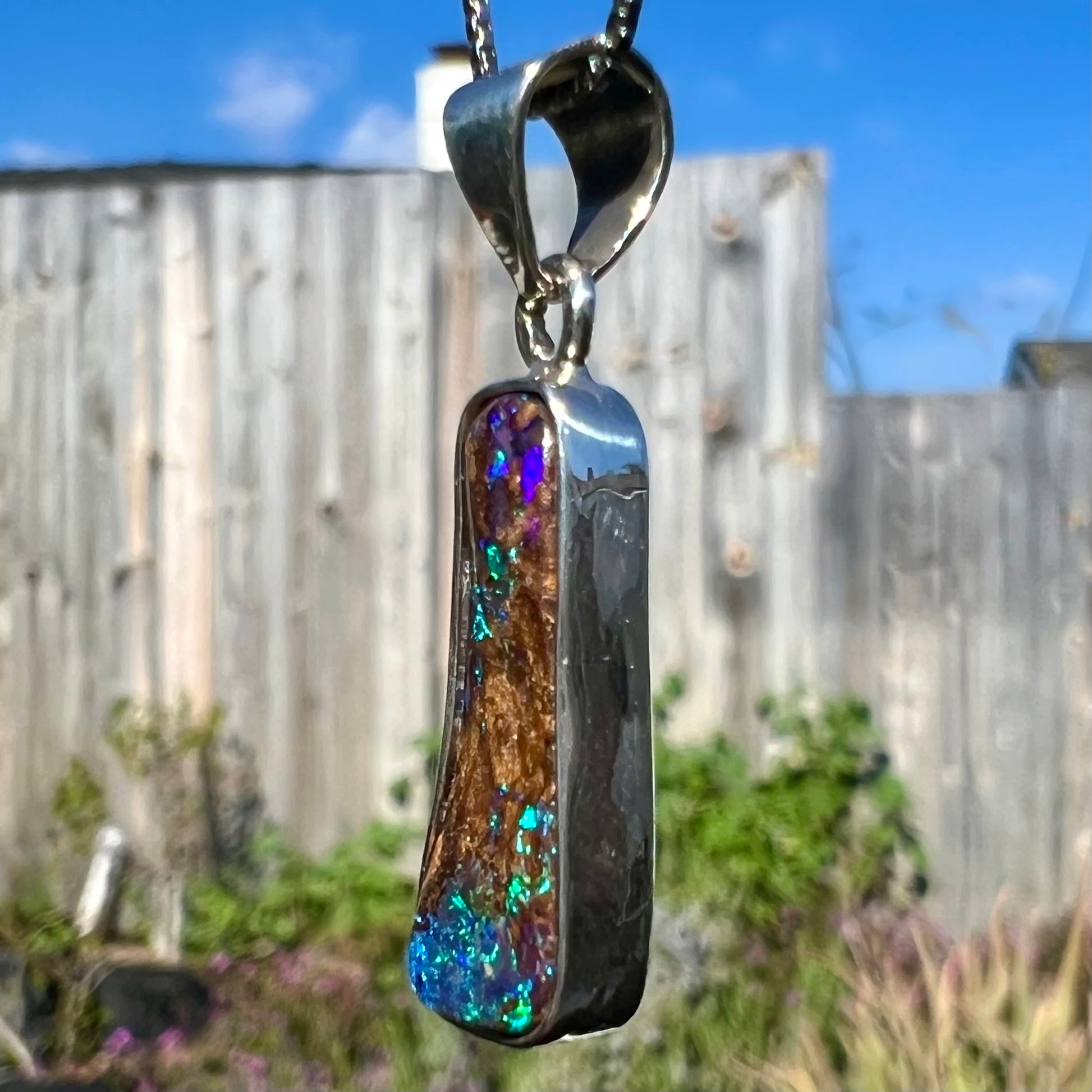 An elongated shaped natural boulder opal necklace in sterling silver.  The opal flashes bright blue and green colors.