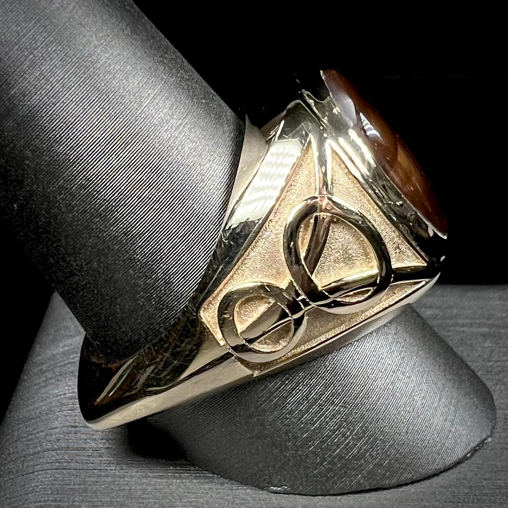 A men's solid yellow gold ring set with a Mexican fire agate stone.  The fire agate has a puple bull's eye pattern.