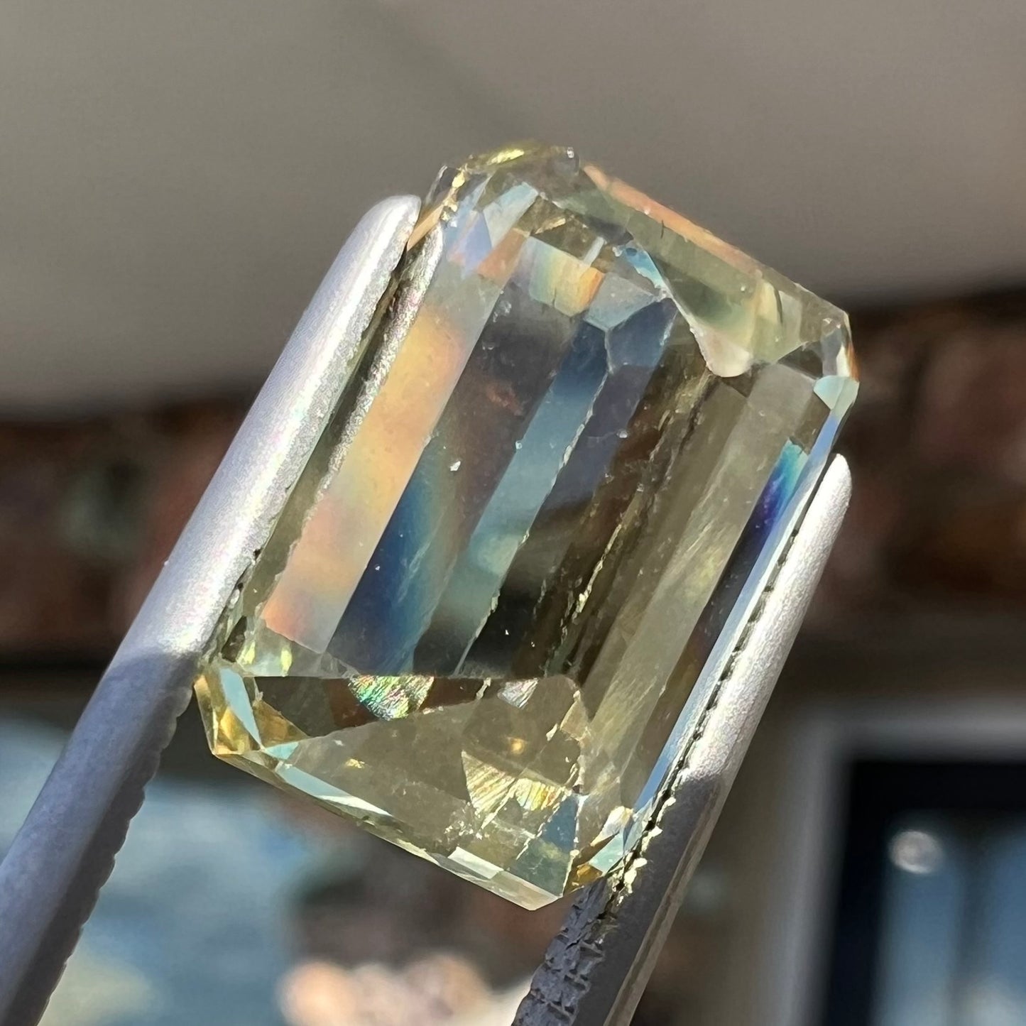 A loose, emerald cut hiddenite gemstone.  The stone is a light yellow green color.