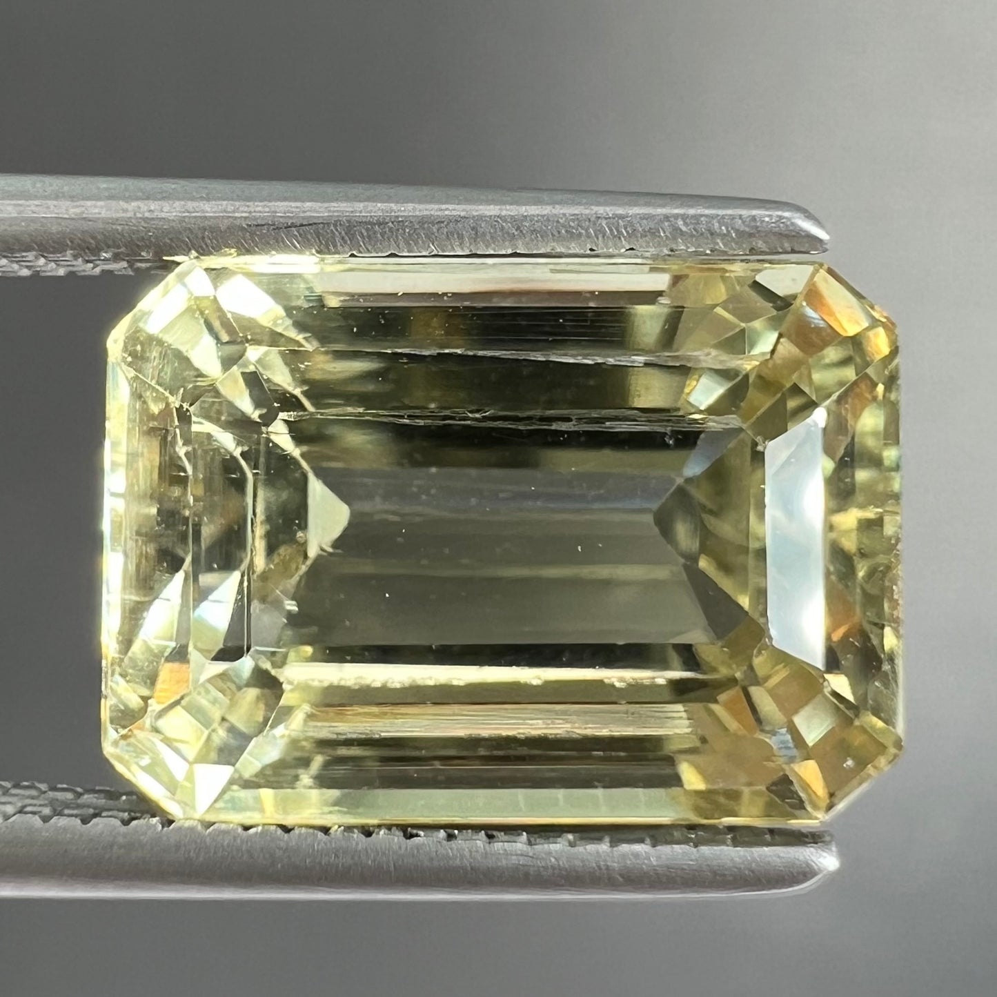 A loose, emerald cut hiddenite gemstone.  The stone is a light yellow green color.