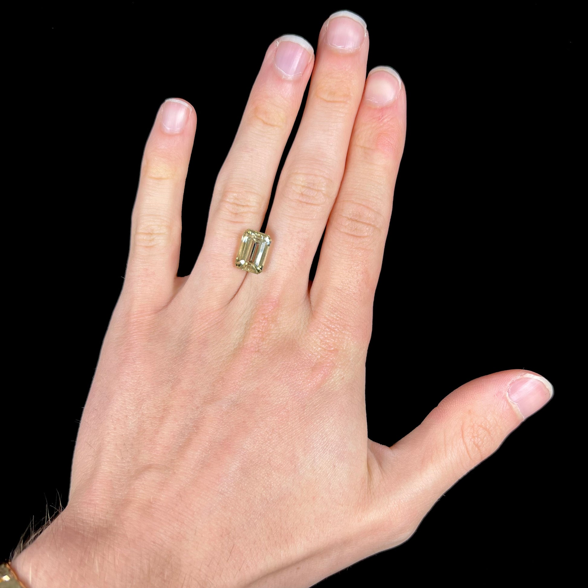 A loose, emerald cut hiddenite gemstone.  The stone is a light yellow green color.
