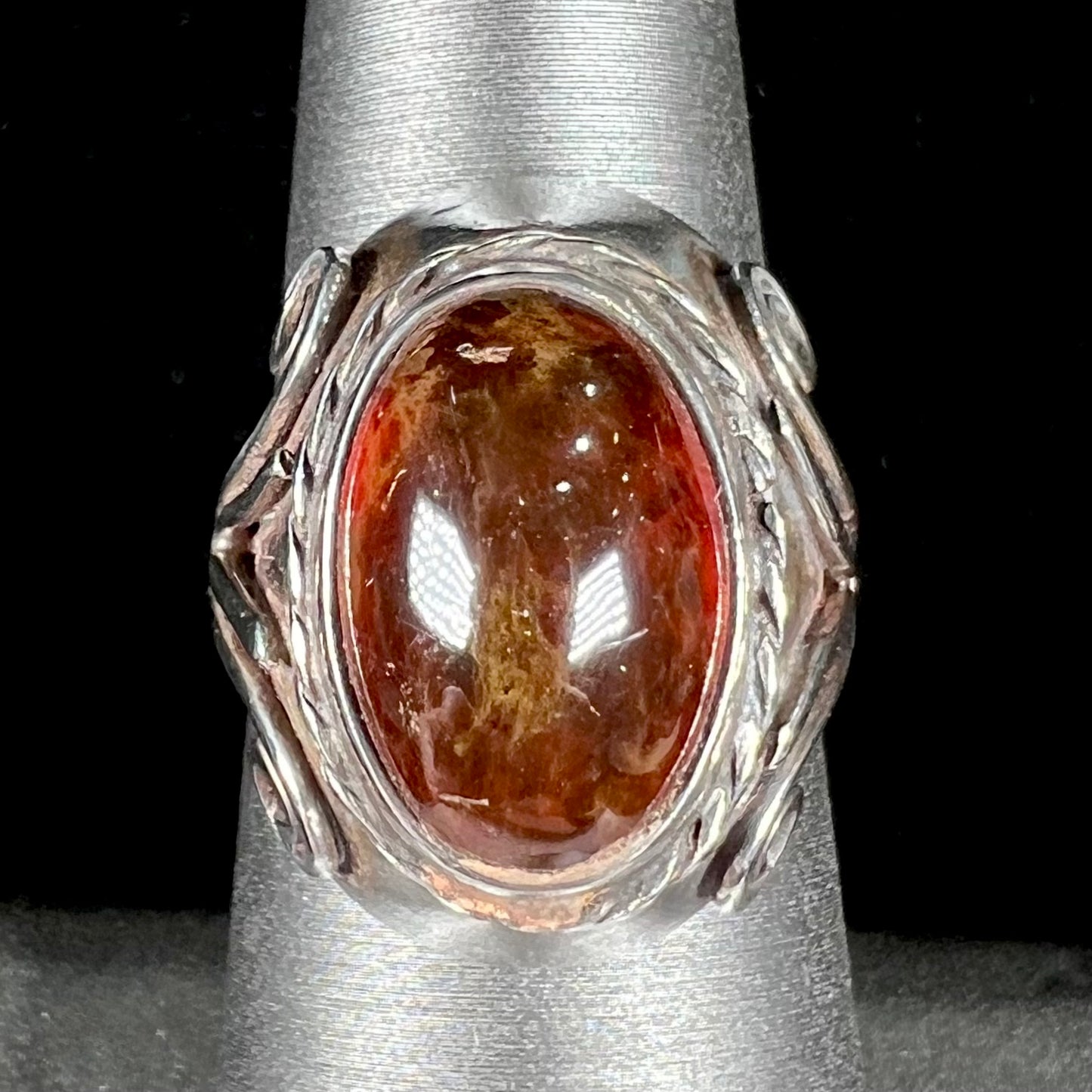 A sterling silver filigree style ring set with an oval cabochon cut red-orange amber stone.