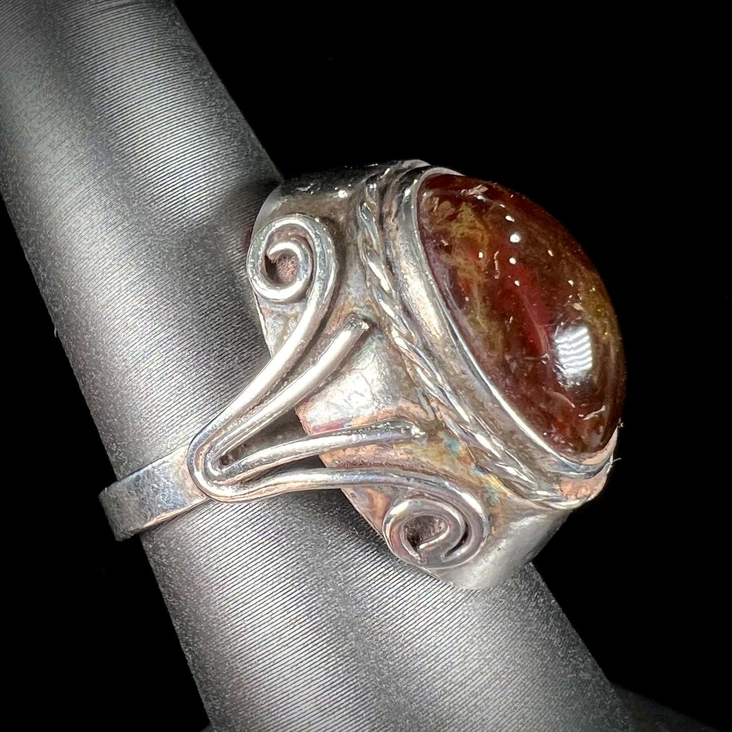 A sterling silver filigree style ring set with an oval cabochon cut red-orange amber stone.