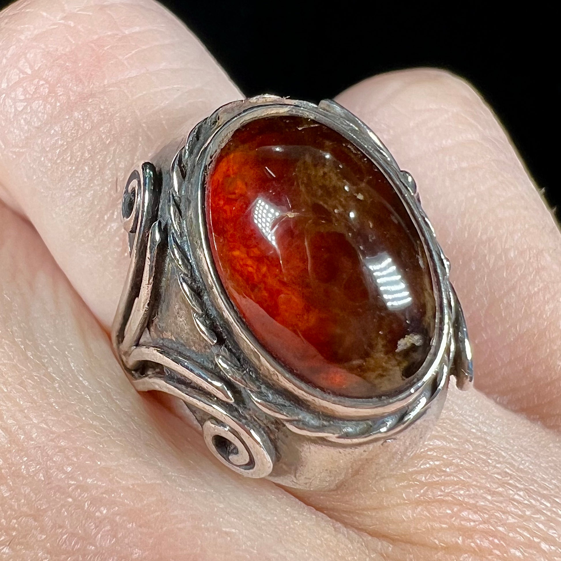 A sterling silver filigree style ring set with an oval cabochon cut red-orange amber stone.