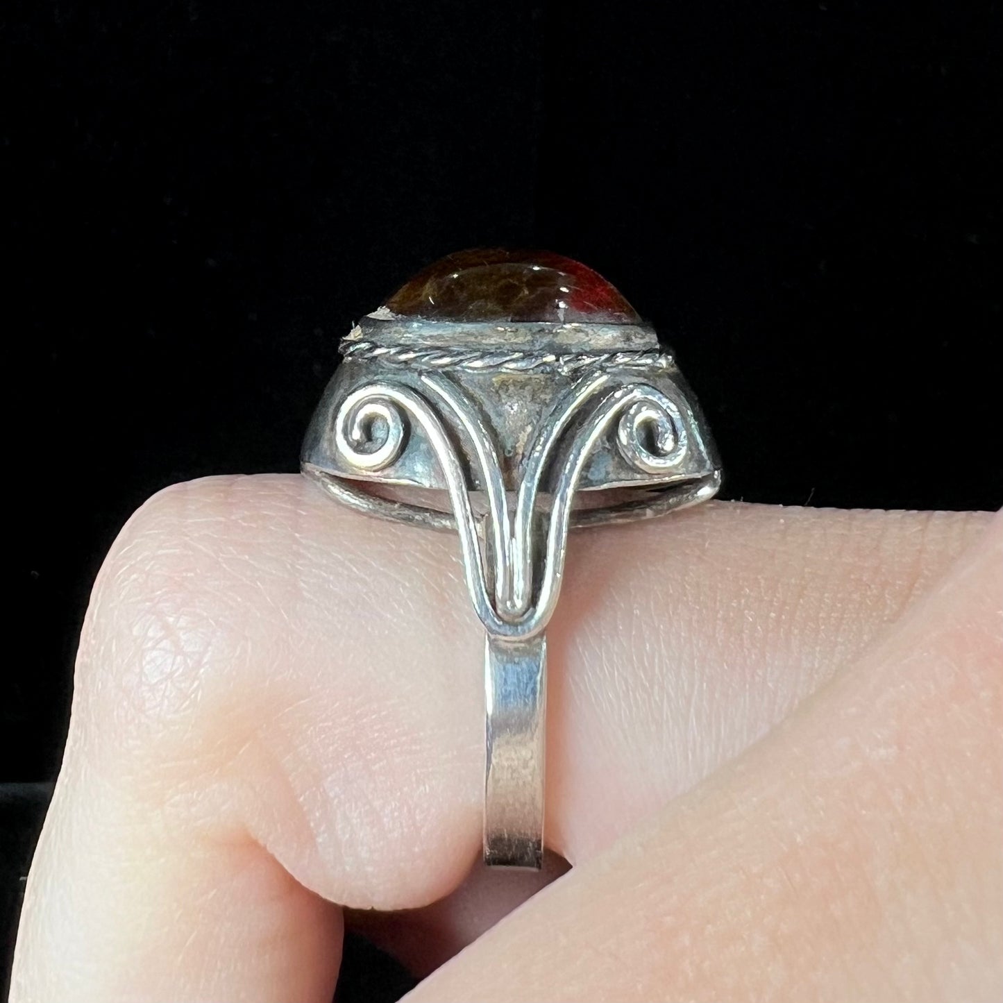 A sterling silver filigree style ring set with an oval cabochon cut red-orange amber stone.