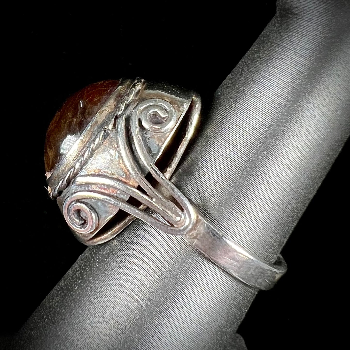 A sterling silver filigree style ring set with an oval cabochon cut red-orange amber stone.