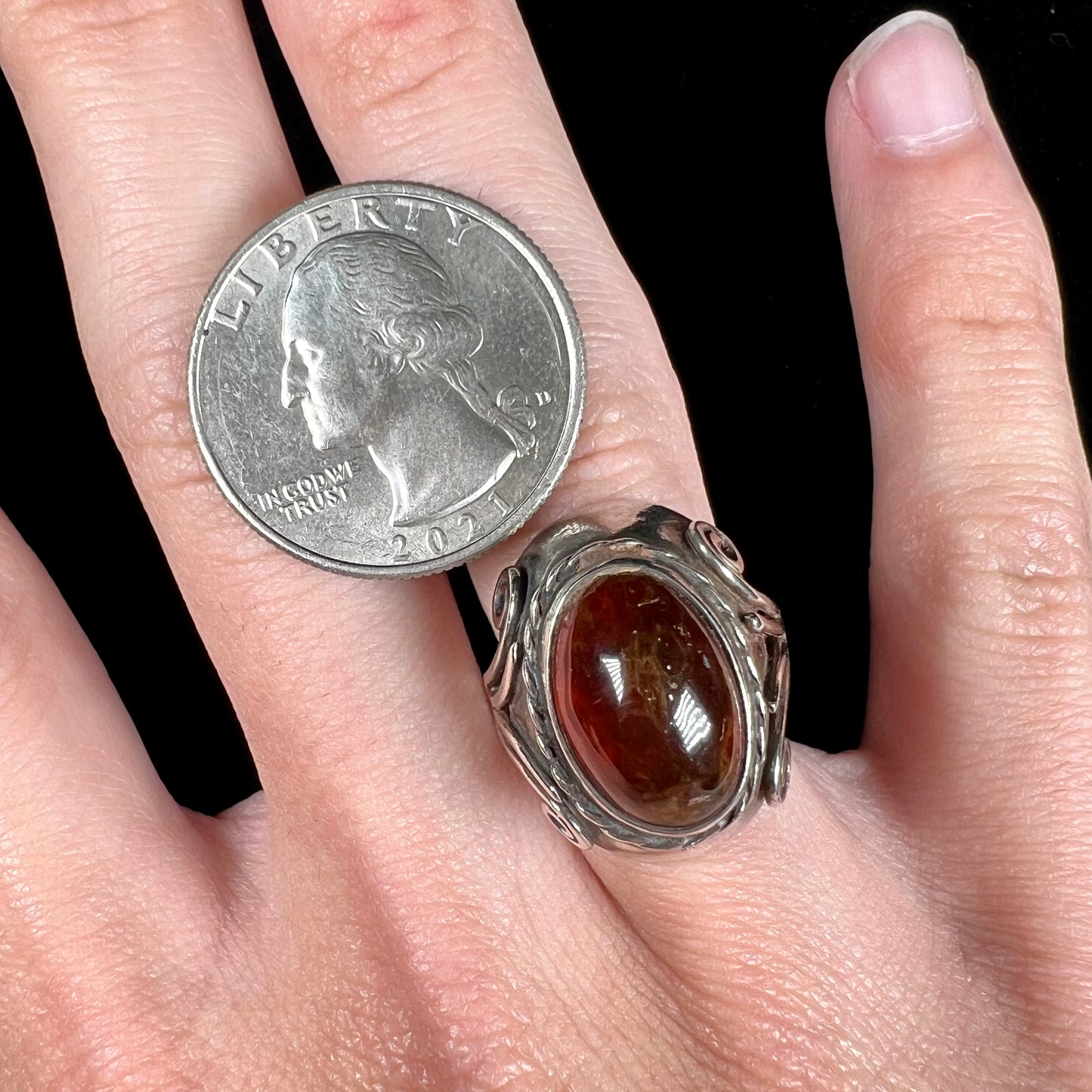 A sterling silver filigree style ring set with an oval cabochon cut red-orange amber stone.