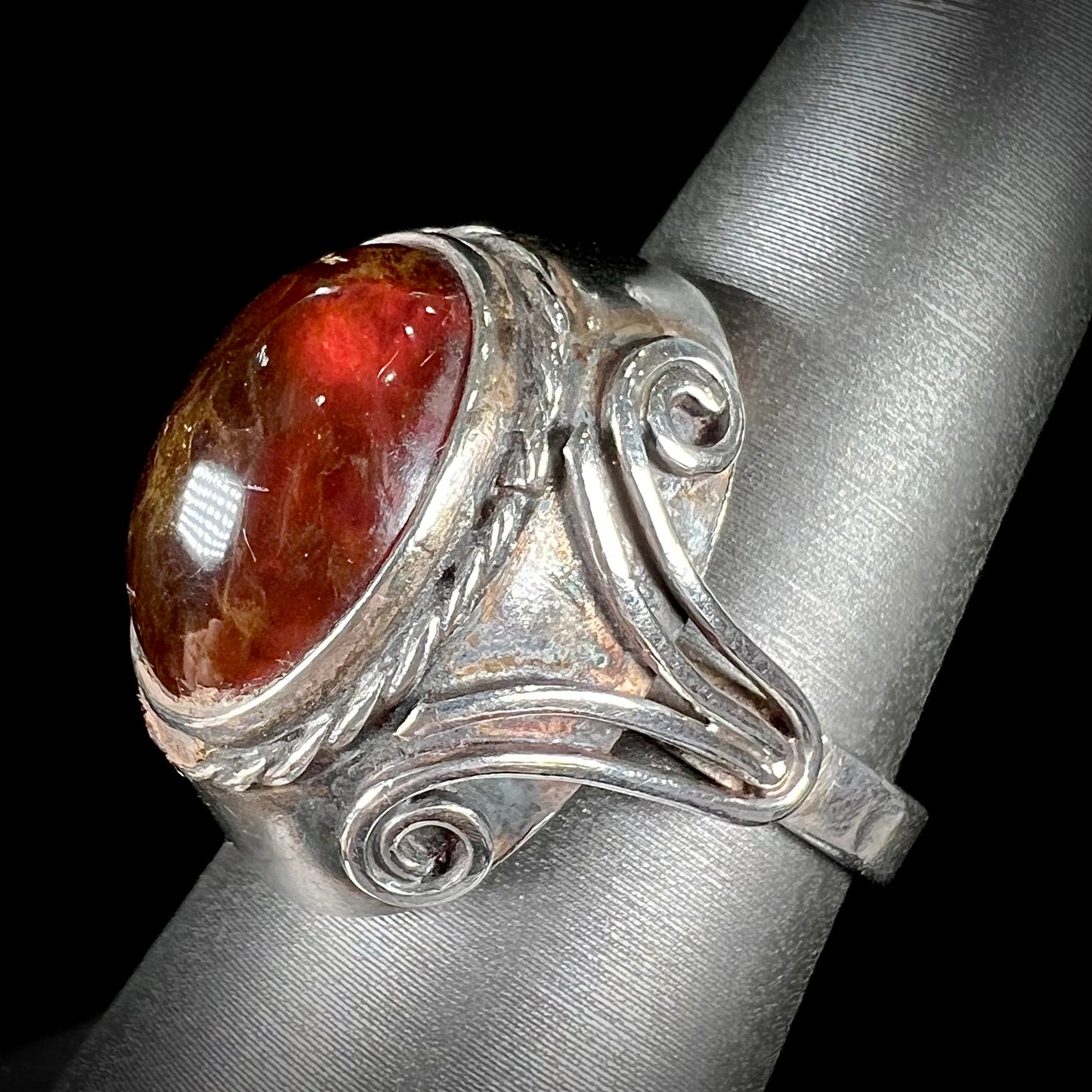 A sterling silver filigree style ring set with an oval cabochon cut red-orange amber stone.