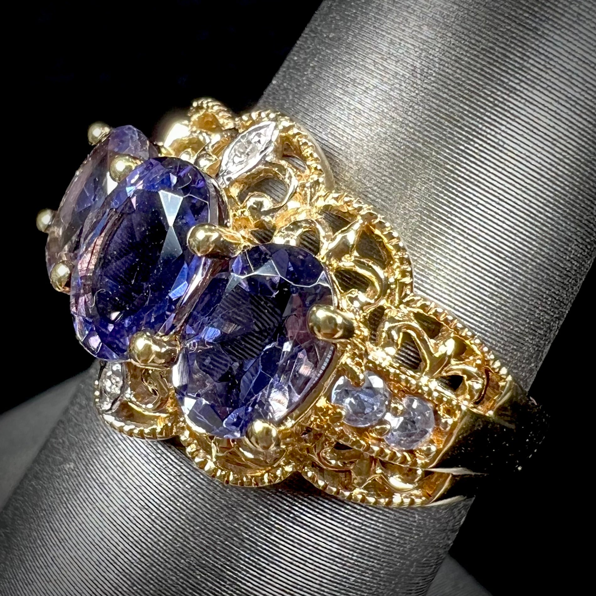 A ladies' three stone iolite ring in yellow gold set with diamond and B grade tanzanite accents.