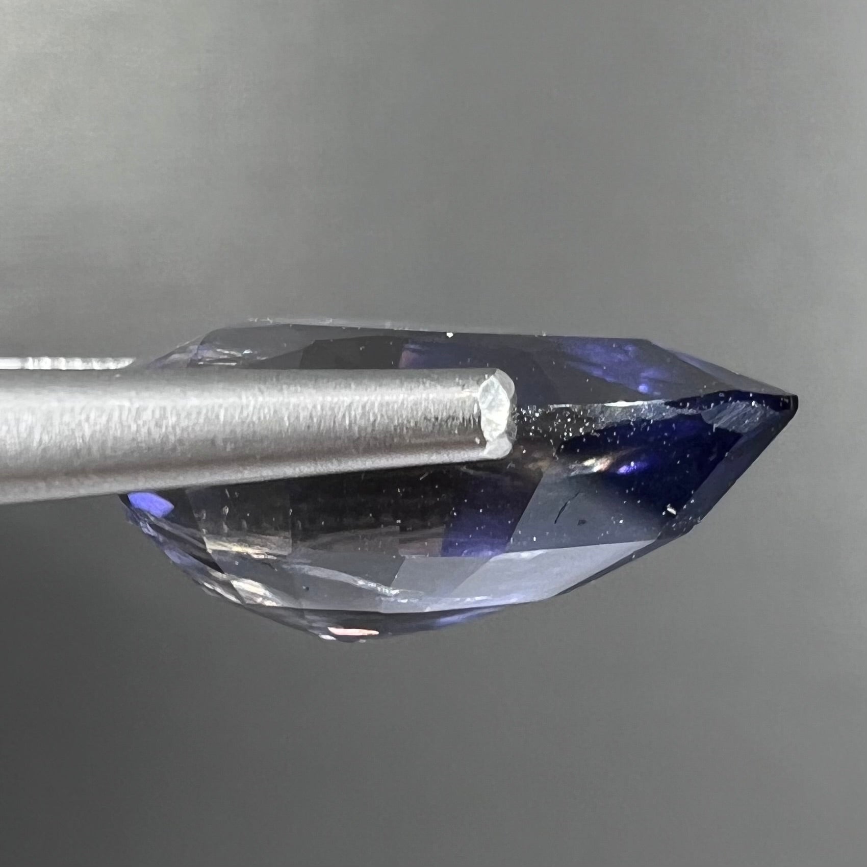 A loose, pear shaped bicolor iolite gemstone.  The stone shows violite purple and silver colors.