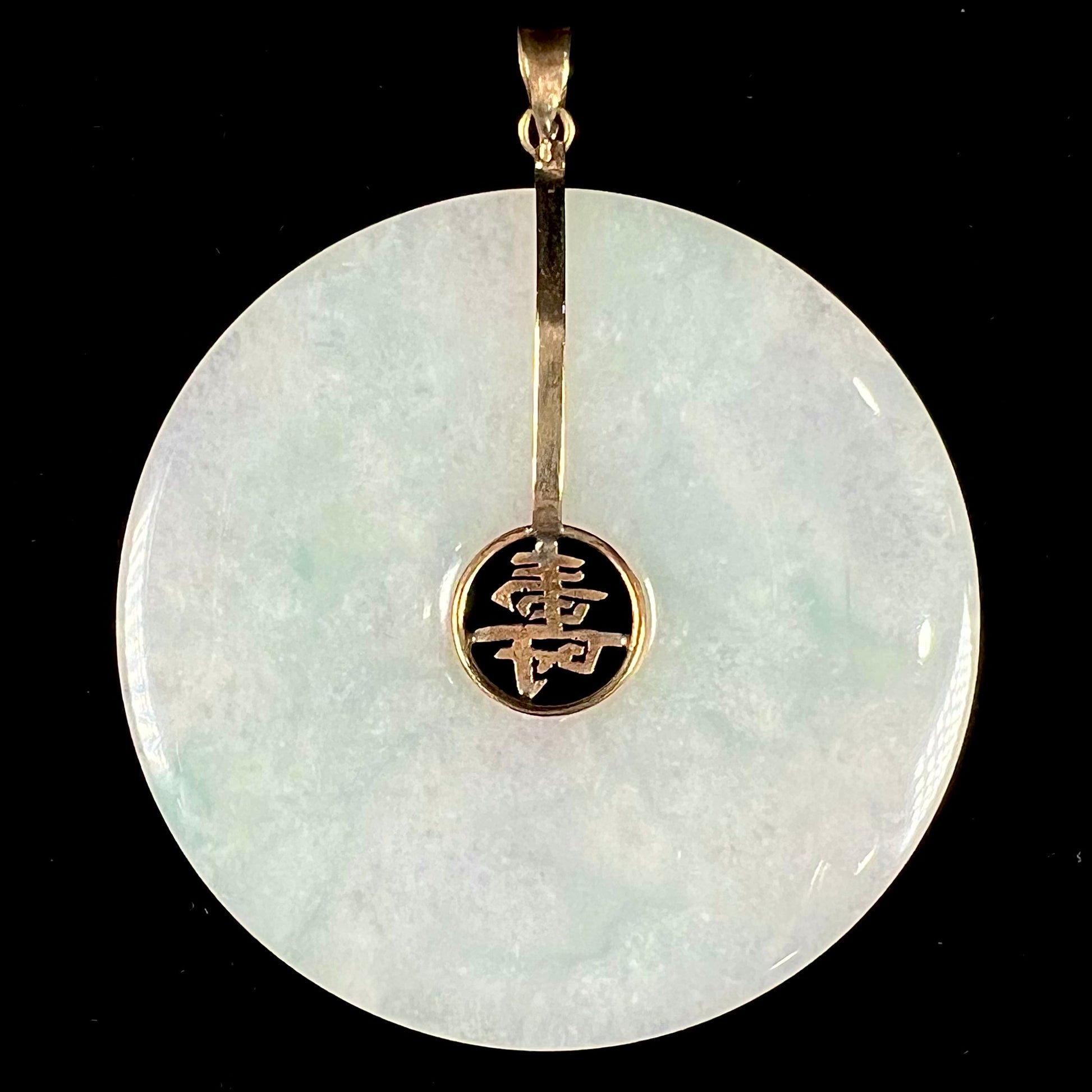 A light green jadeite jade bi pendant with a yellow gold bail and Chinese character symbol for "long life."