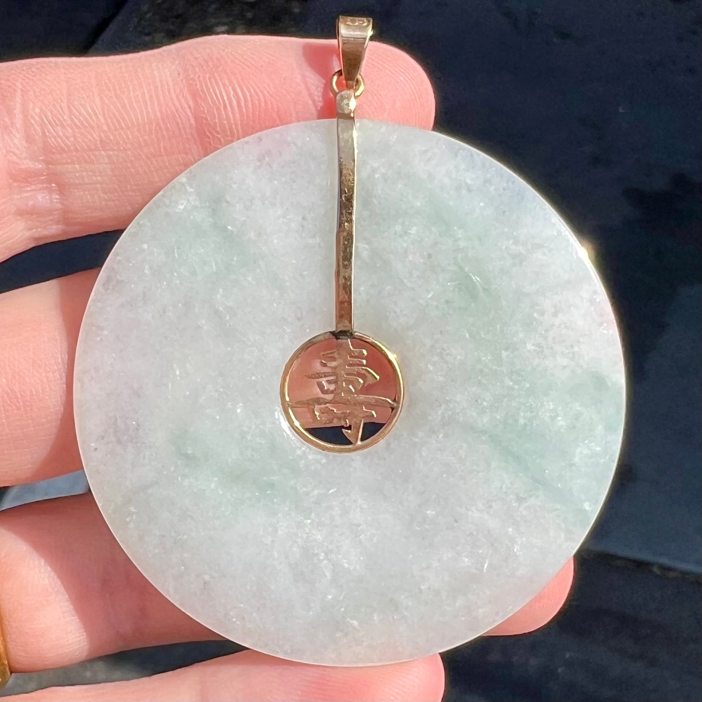 A light green jadeite jade bi pendant with a yellow gold bail and Chinese character symbol for "long life."