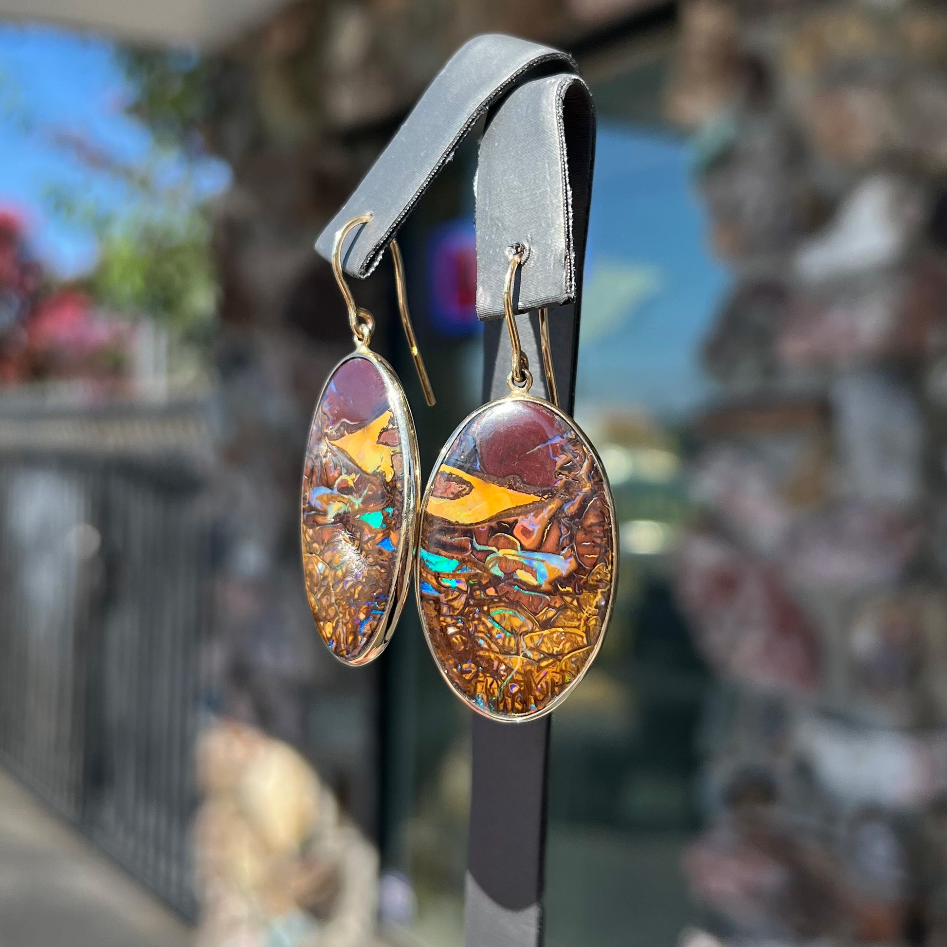 A pair of oval cut Koroit boulder opal dangle earrings in yellow gold bezel frames.  The opal exhibits a unique pattern and blue colors.